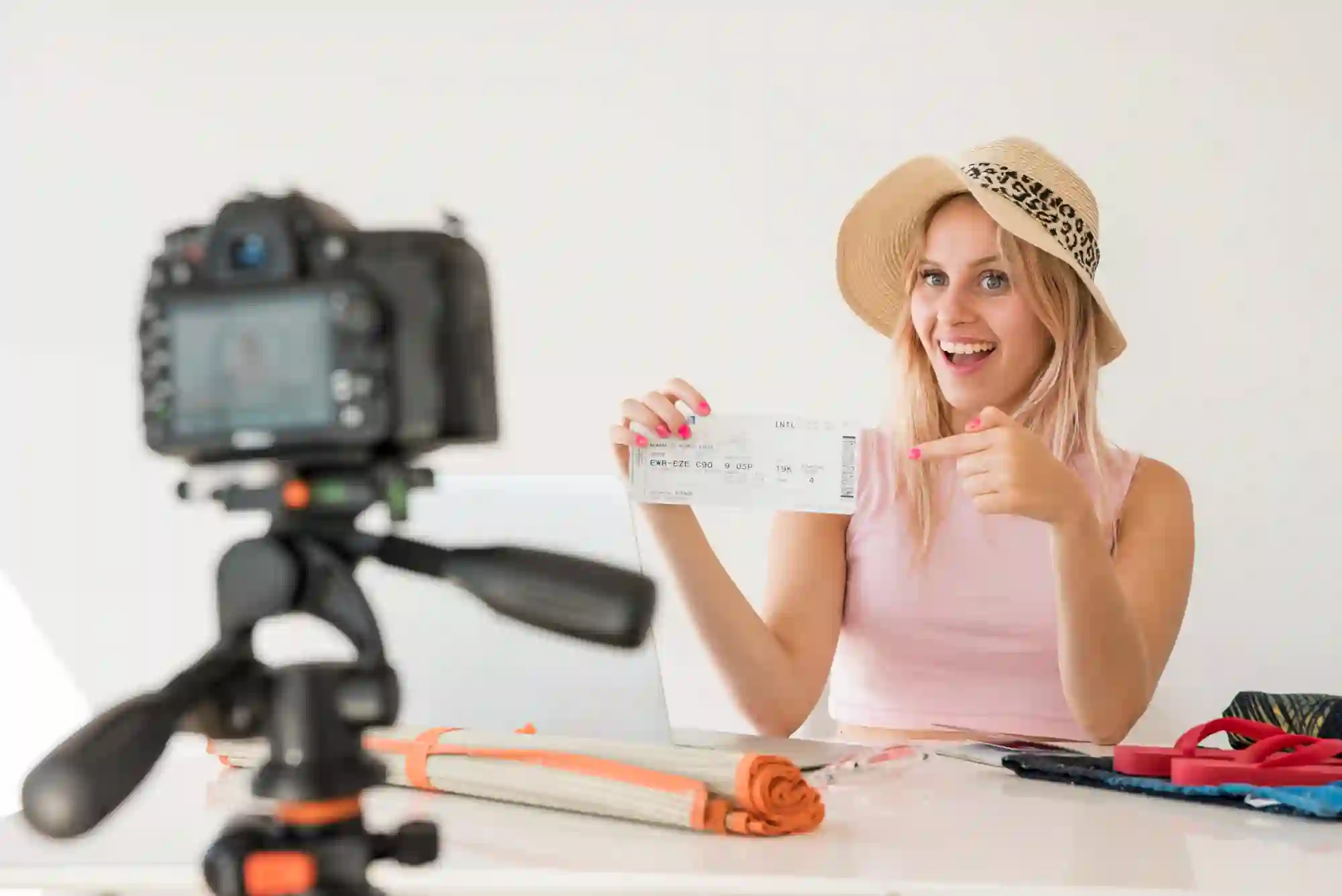 A vlogger is filming herself with a camera while holding up an airplane ticket.