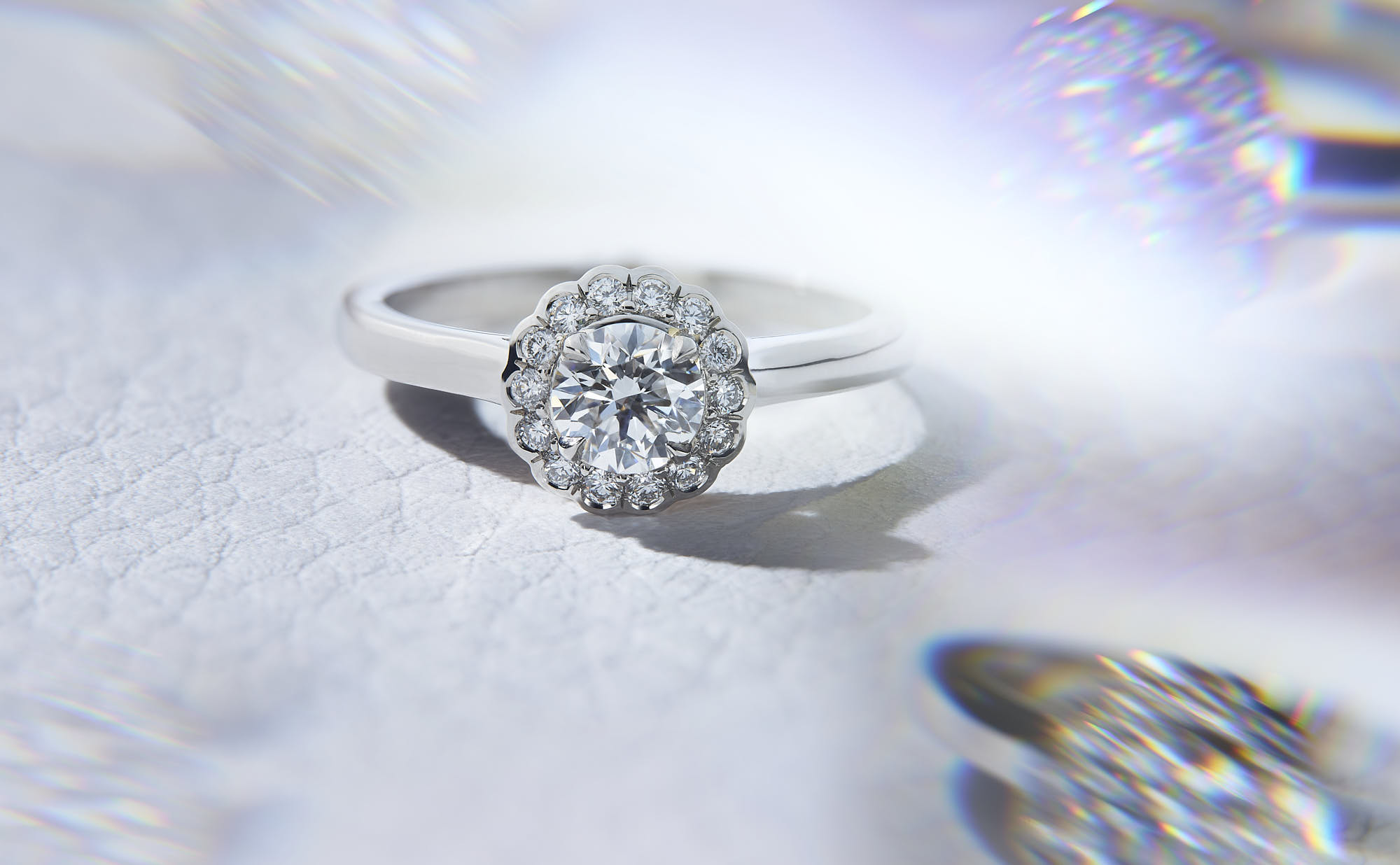 Elegant diamond engagement ring with halo setting on white surface.
