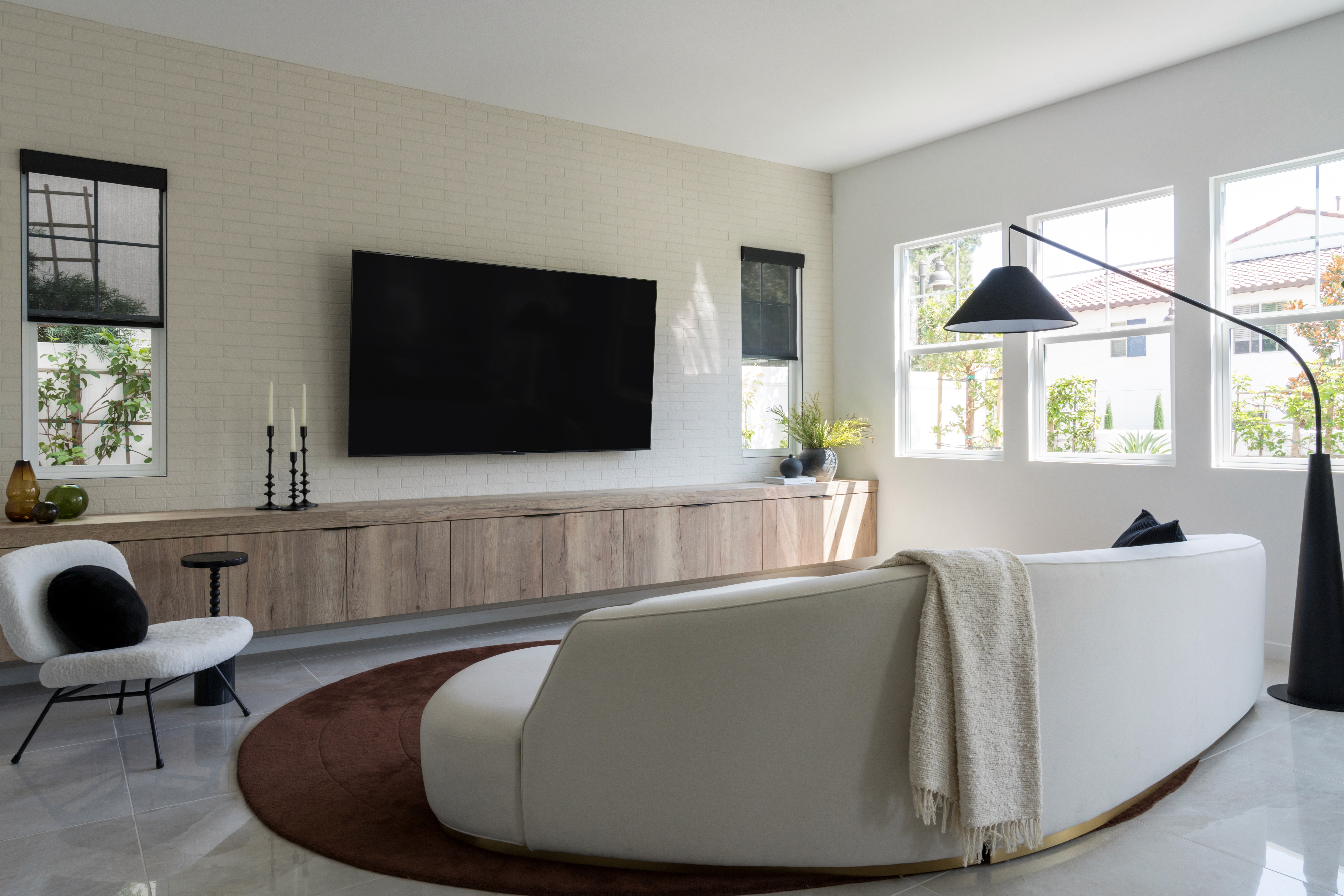 Mid century modern living room with white kidney bean couch, neutral wood media console, warm brown rug, white brick accent wall, and black brass floor lamp by Jubilee Interiors in Arcadia, California