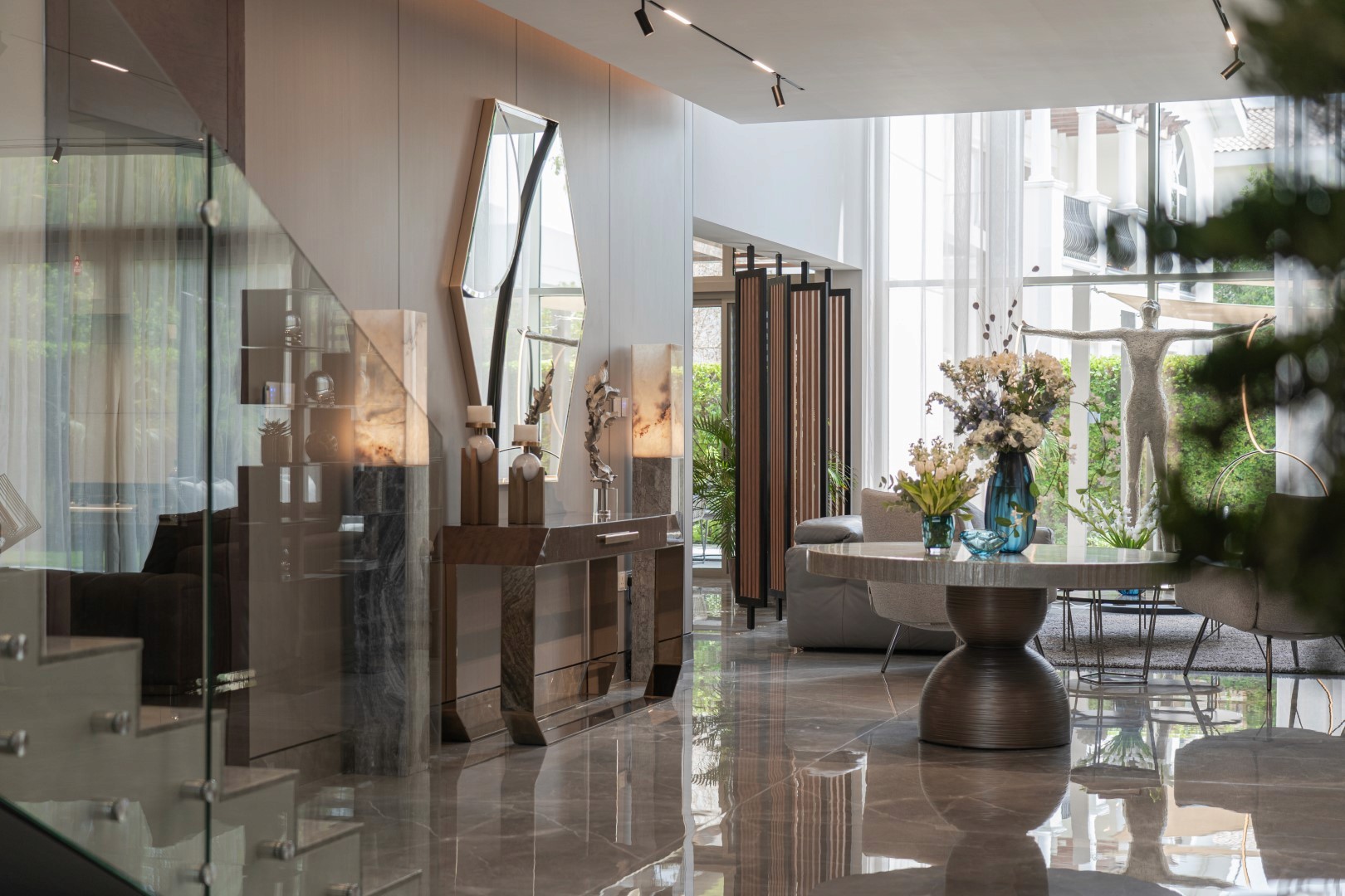 Modern living room interior with large windows, a sleek staircase, decorative mirrors, and stylish furniture, creating a spacious and elegant ambiance.