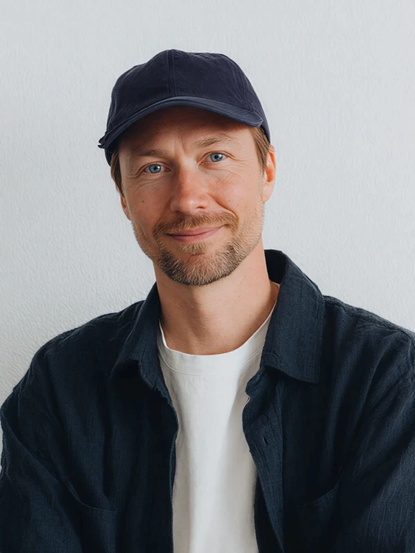 A person wearing a black cap and jacket smiles, posing against a light background.