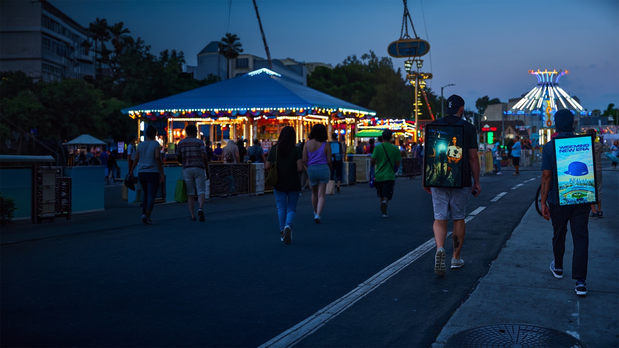Two Wunderparks carriers walking a closed street at dusk past lit fairground rides