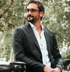 Professional photo of Rob Stewart wearing sunglasses and a grey suit jacket in an outdoor setting with trees in background