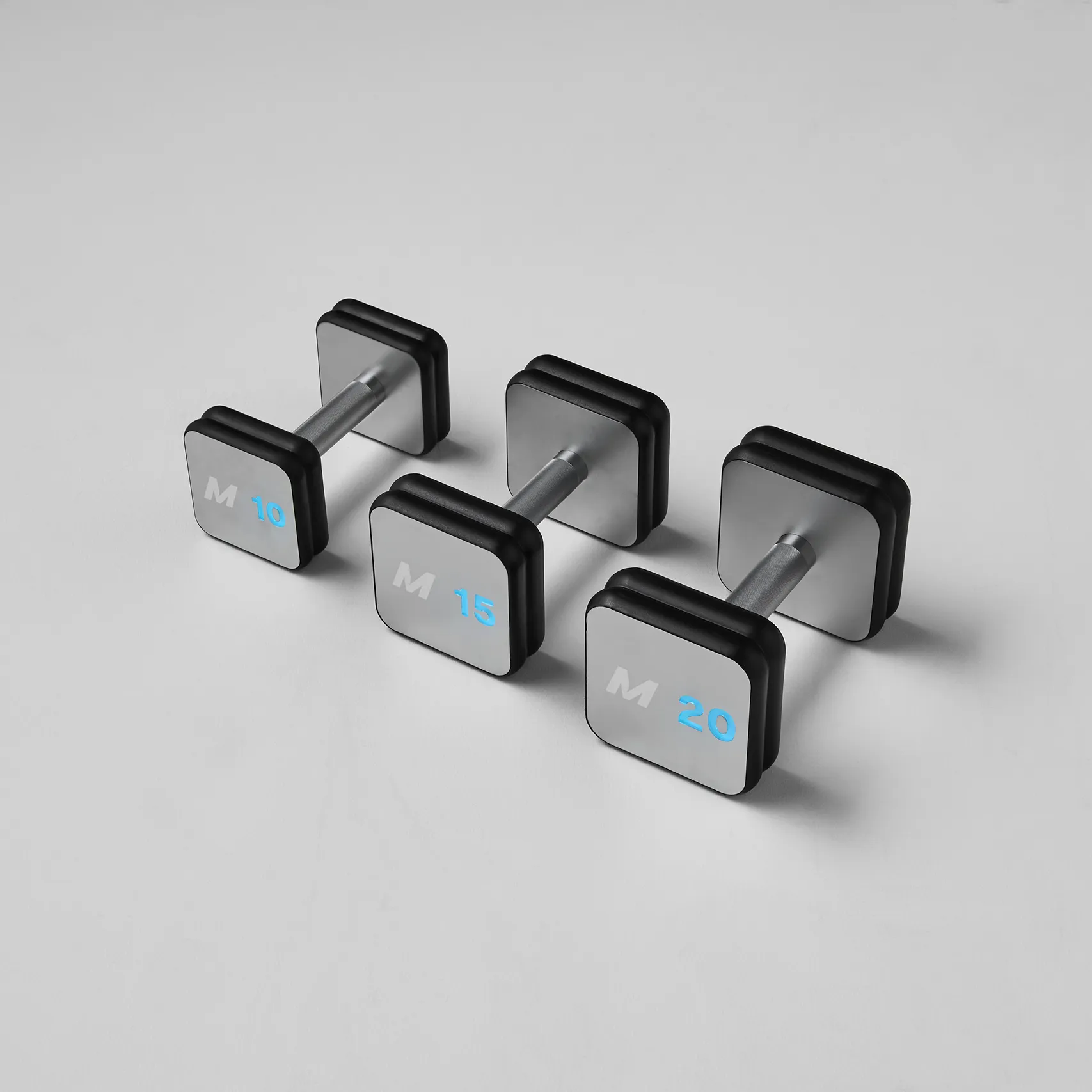 Three connected Mirror smart dumbbells with illuminated weight indicators on gray