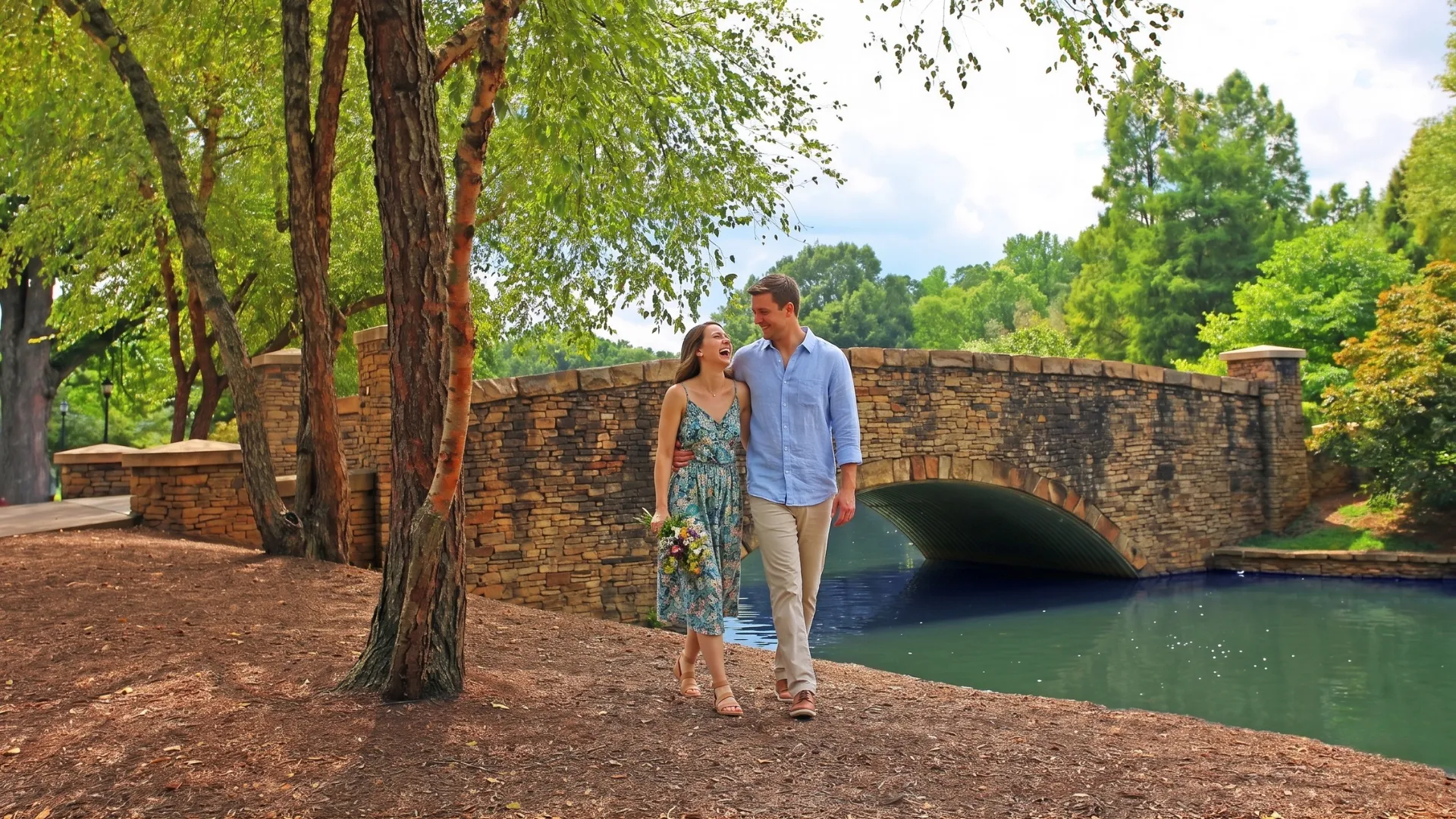 A couple smiles for a photo in front of a large bridge, showcasing their happiness and the scenic backdrop.