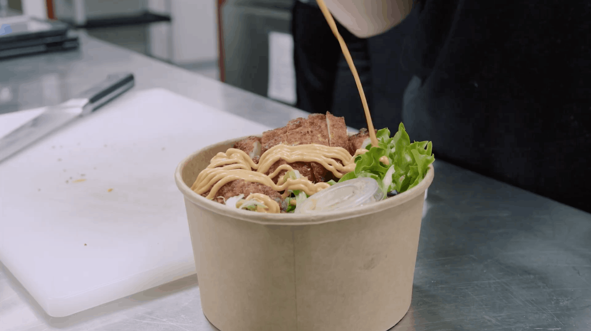 chef pours salad dressing onto a bowl of salad in their cloudkitchen