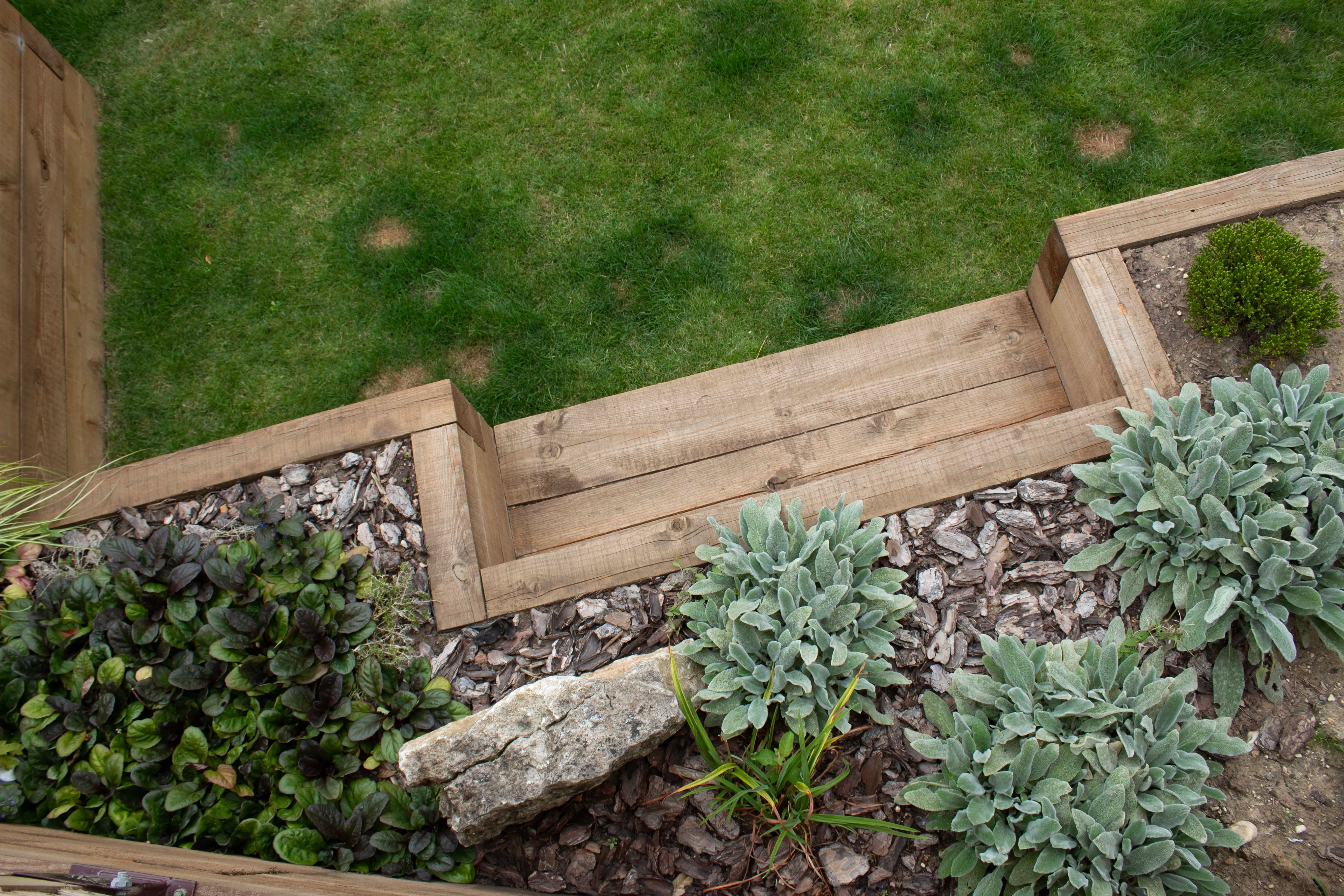 Aerial view of a garden pathway bordered by green grass and plants, featuring wooden edging and stone decoration.