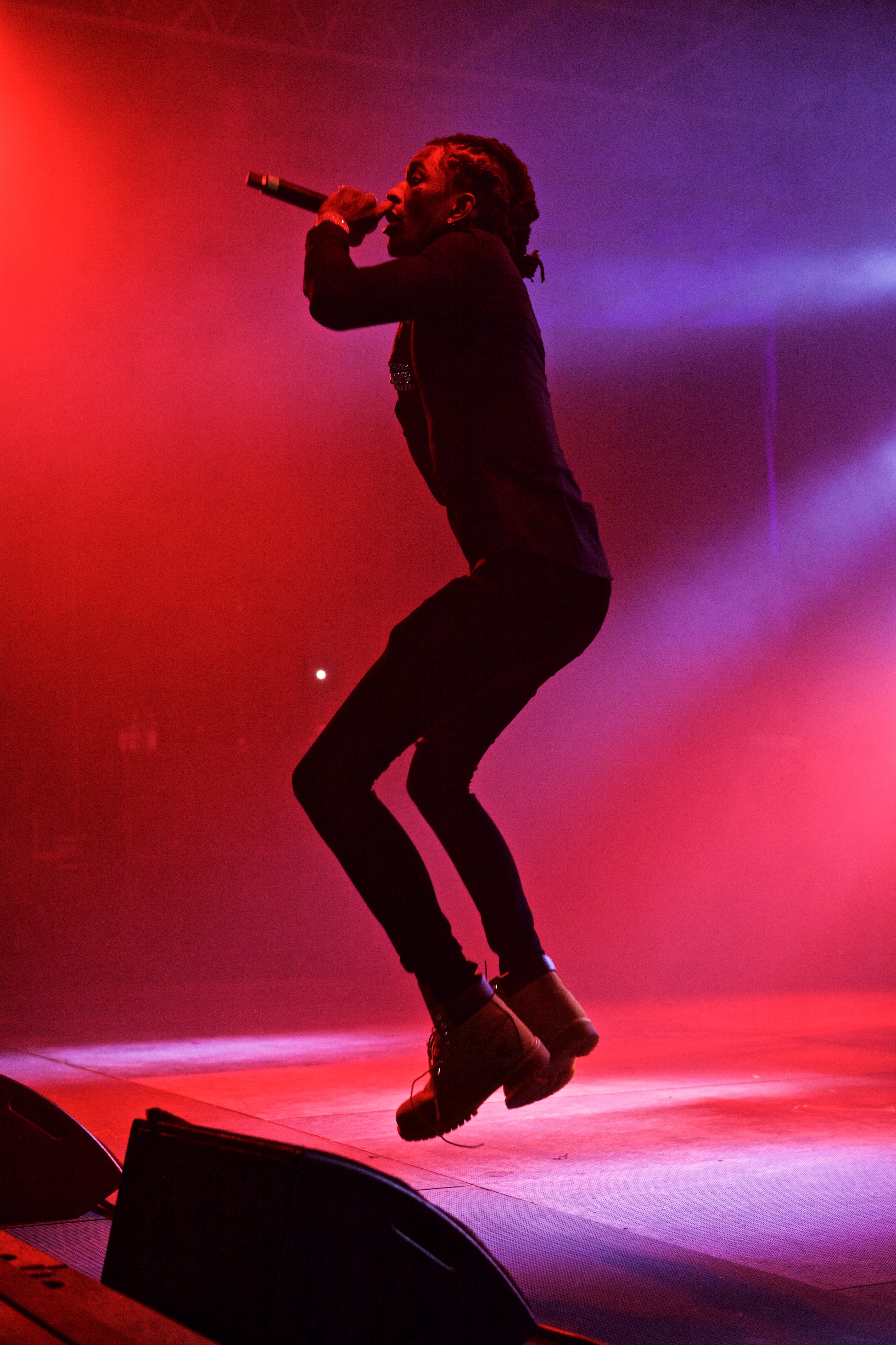 Young Thug caught mid-jump onstage in red lighting during a live concert.