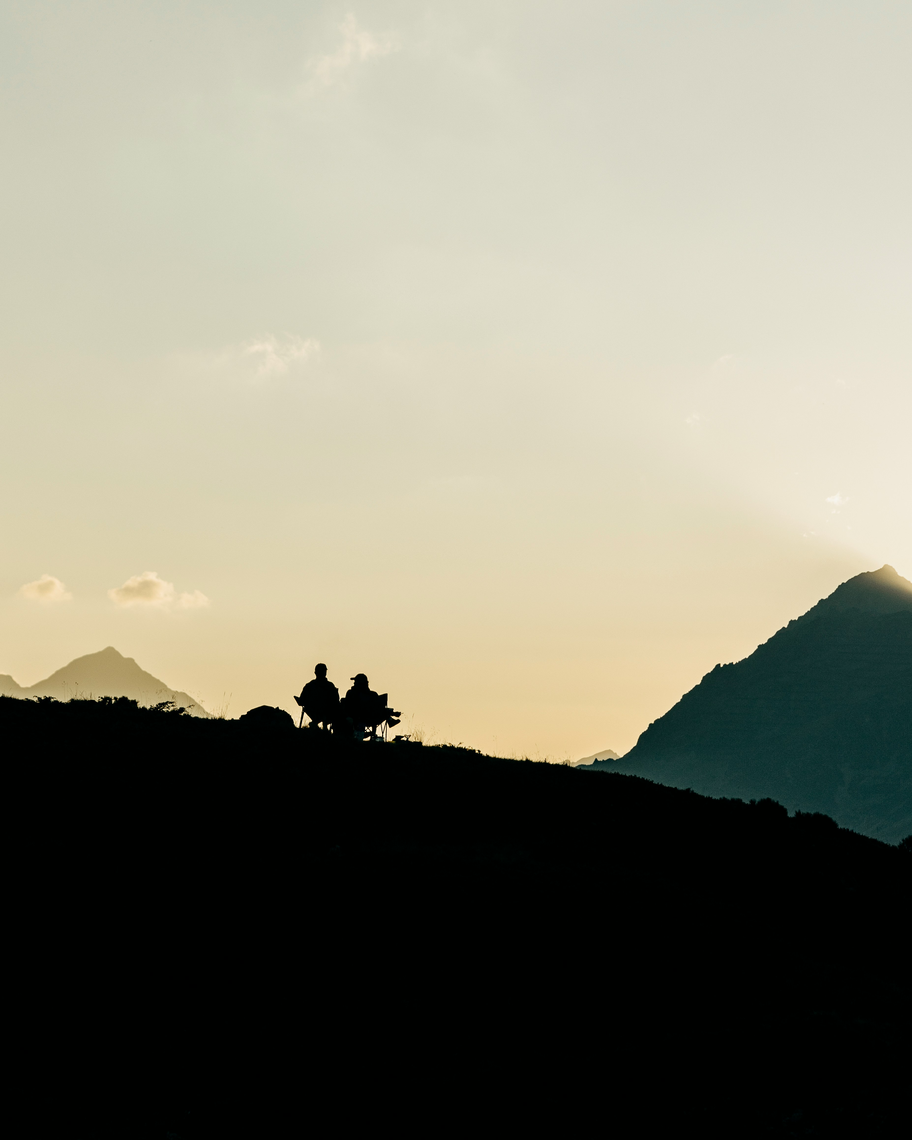 Two people silhouetted on a mountain ridge at sunset.