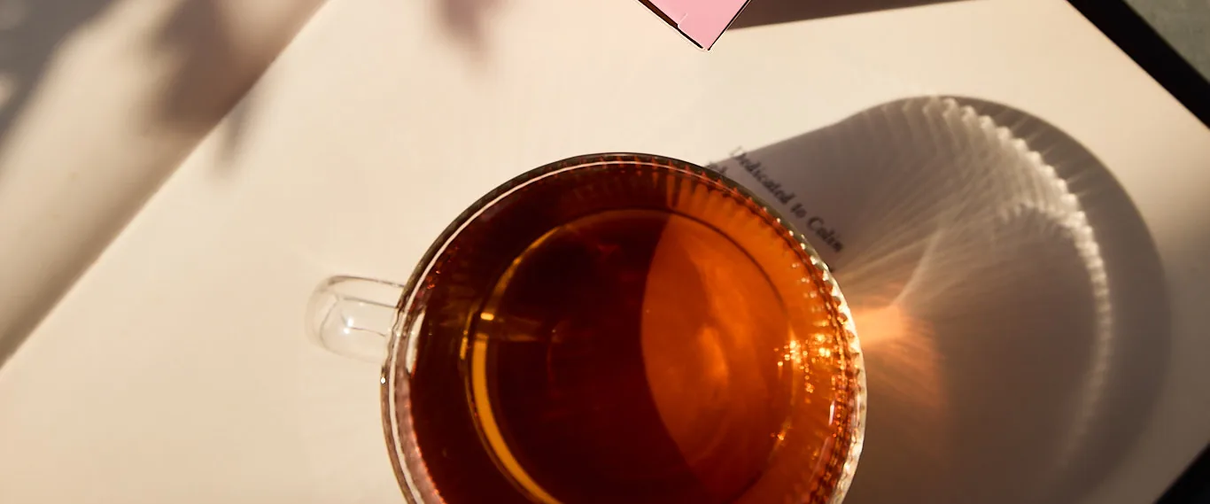 A glass cup of Sēkret tea on paper in dappled afternoon light