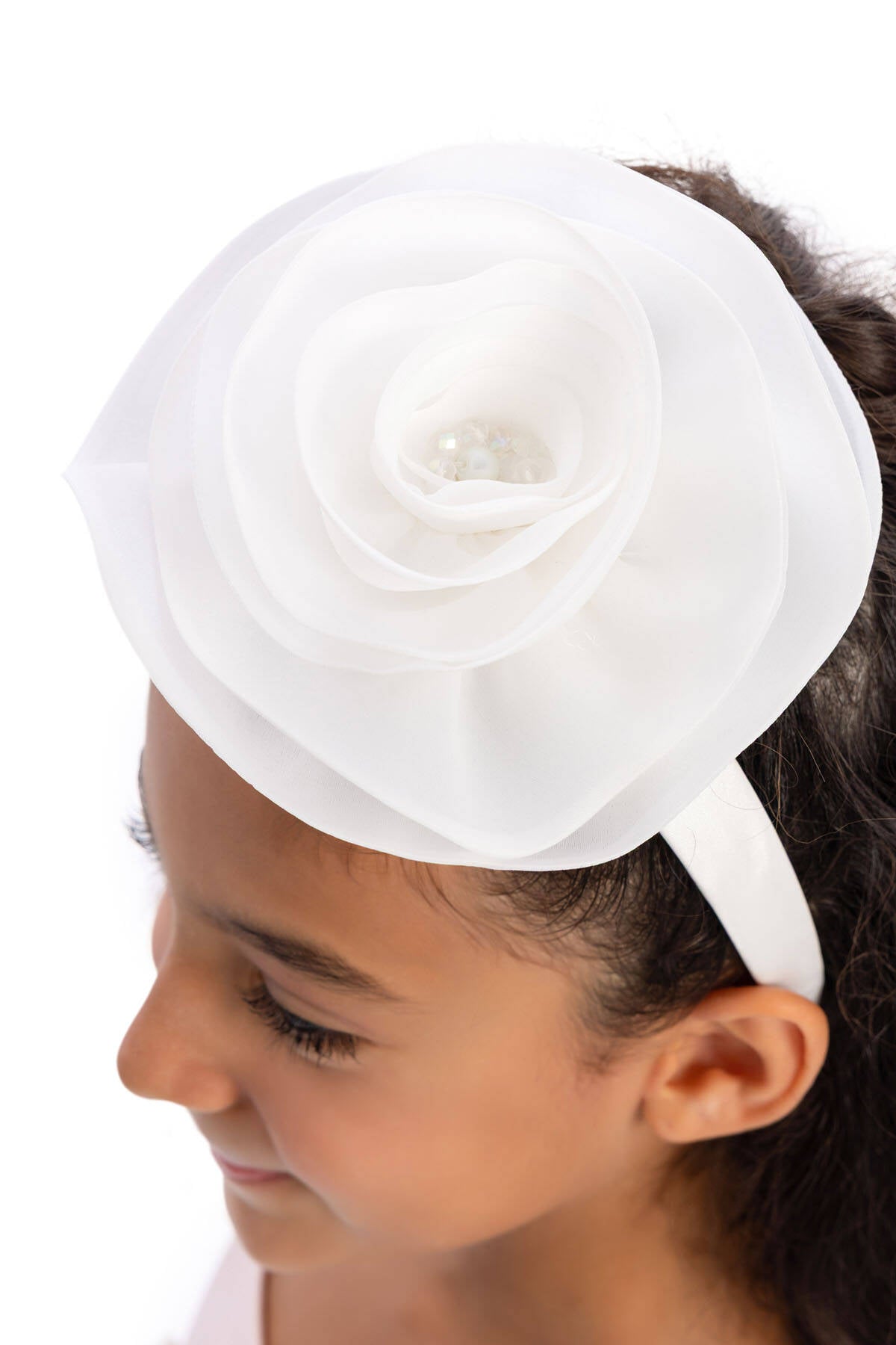 White headband with a large flower on a child's head against a white background