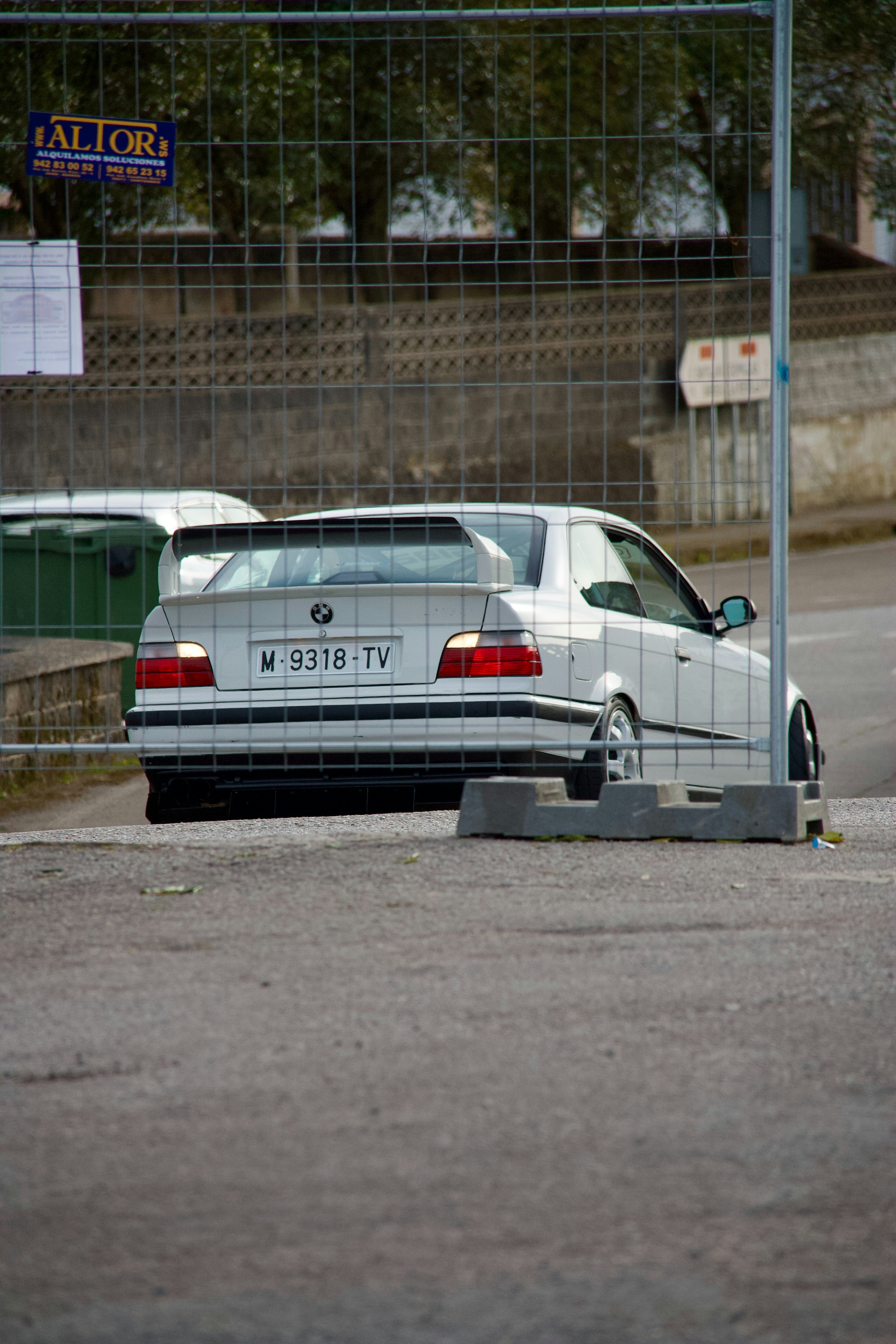 a white car parked in a parking lot next to a fence