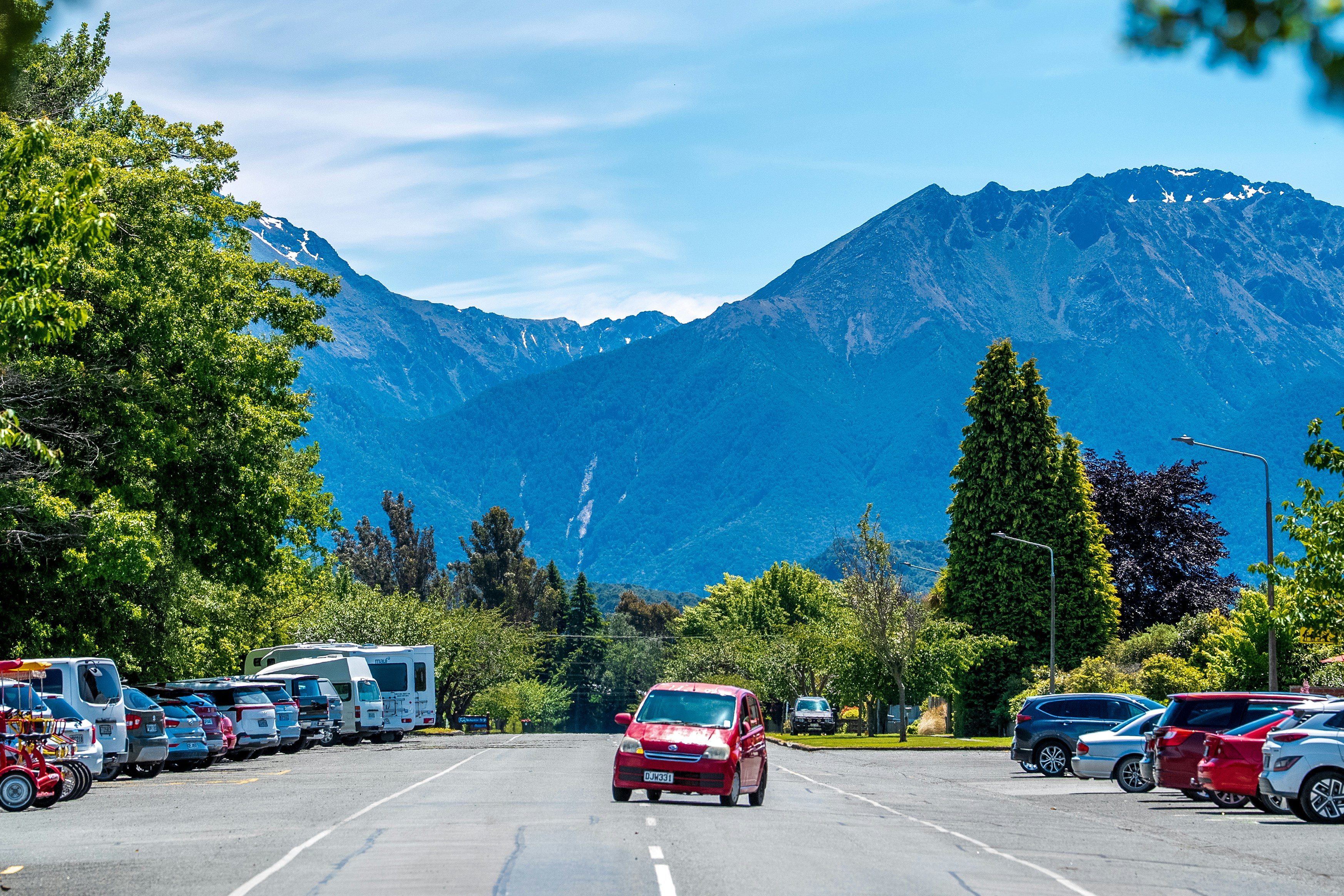 A red car driving down a street next to a forest