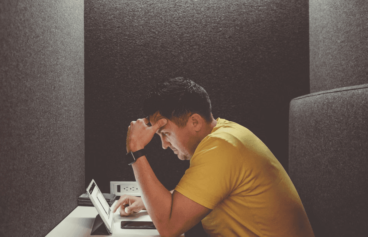 A man sitting in an office booth, leaning forward with his head resting on his hand while looking at a tablet screen