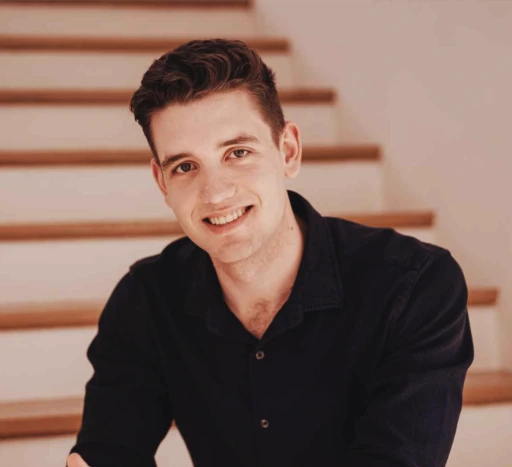 Cornelius Weidmann Webdesign sitzt mit Hemd auf einer Treppe und lächelt