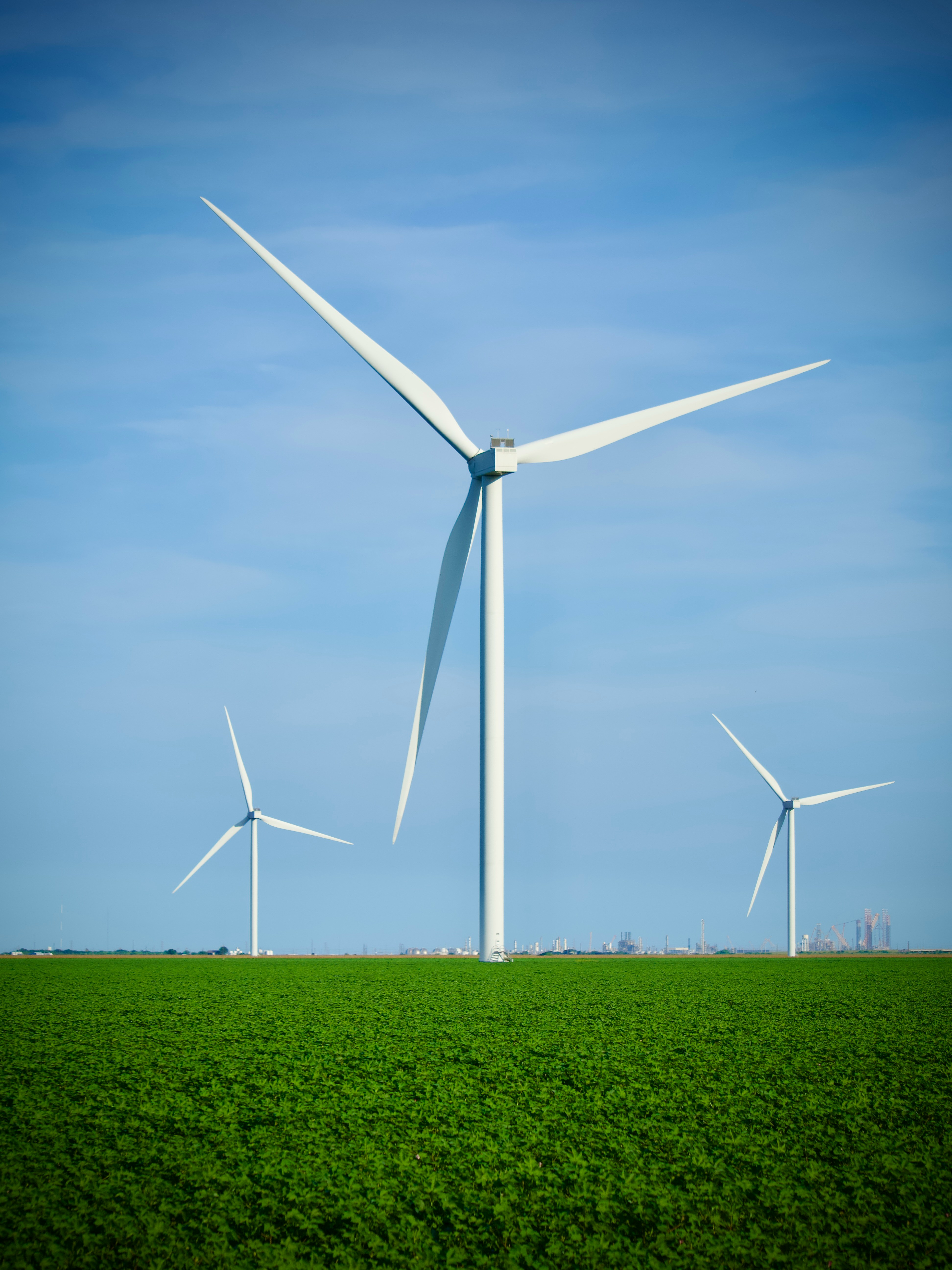 three wind turbines in a green field with a blue sky in the background