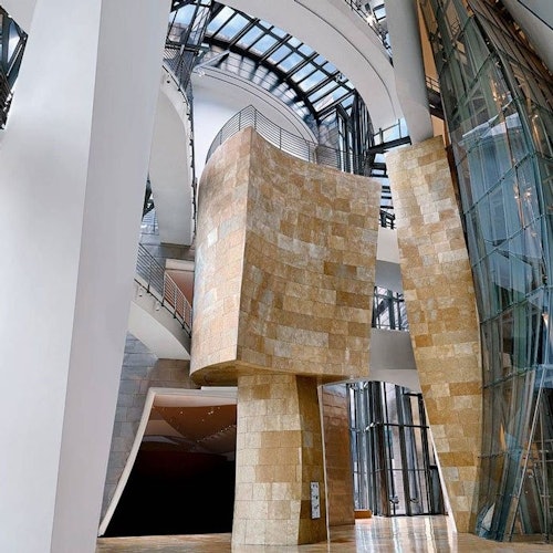Modern interior with curved stone and glass structures, high ceilings, and a mezzanine with metal railings.