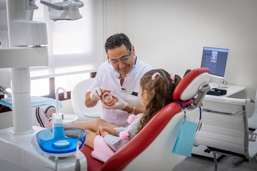Family dentist at Bella Medical Centre showing a teeth model to a young pediatric patient.