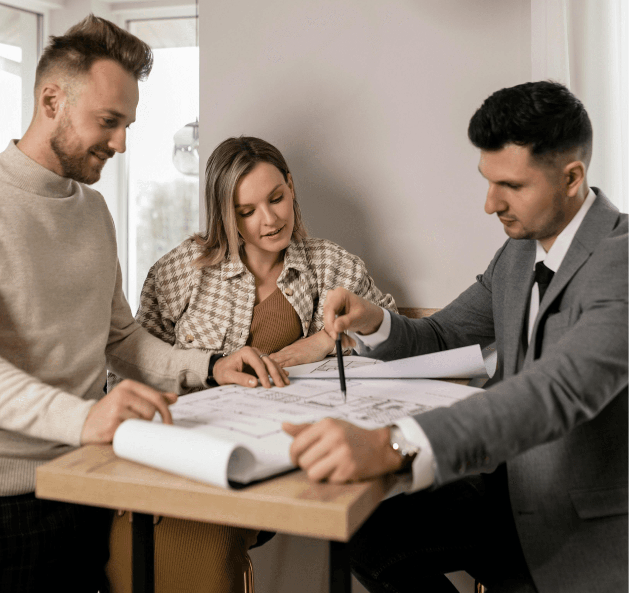 Three people engaged in a discussion around a table with plans and documents, focused on their work.