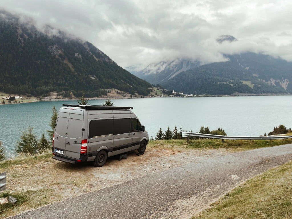 ein grauer Van steht vor einem see und im hintergund sind berge