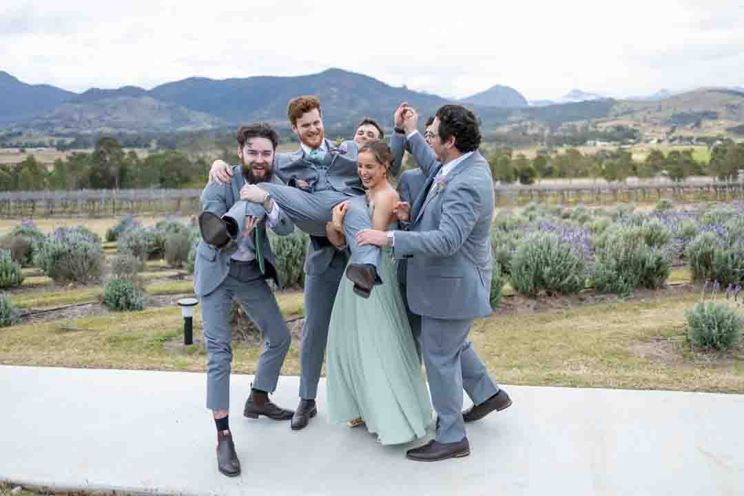 Groomsmen and bridesmaid lifting groom in front of lavender field