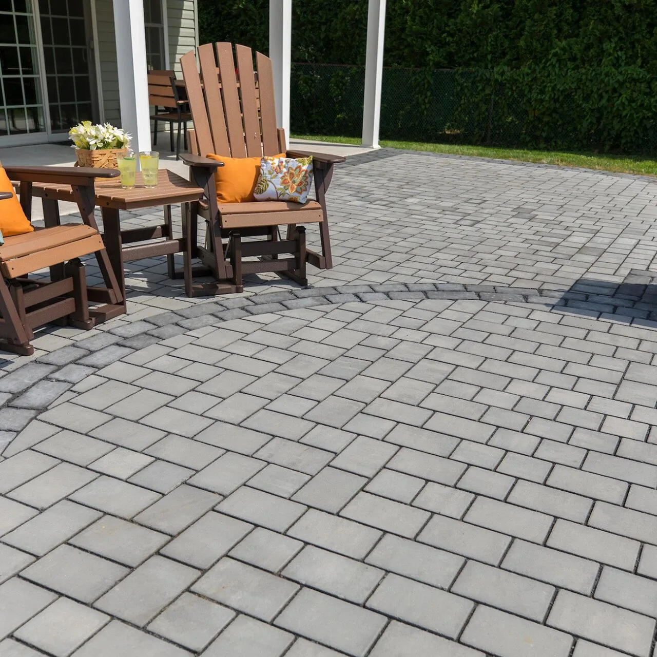 Space for everyday use Gray interlocking paver patio with wooden chairs outside a home.