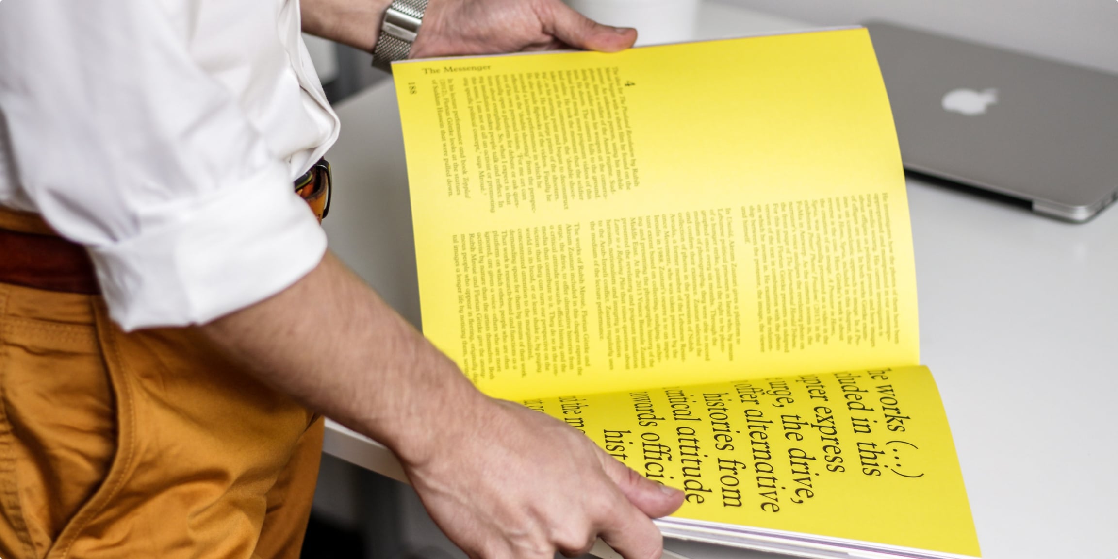 Decorative image of the lower trunk of a man holding a colorful book with yellow pages and typographic elements.