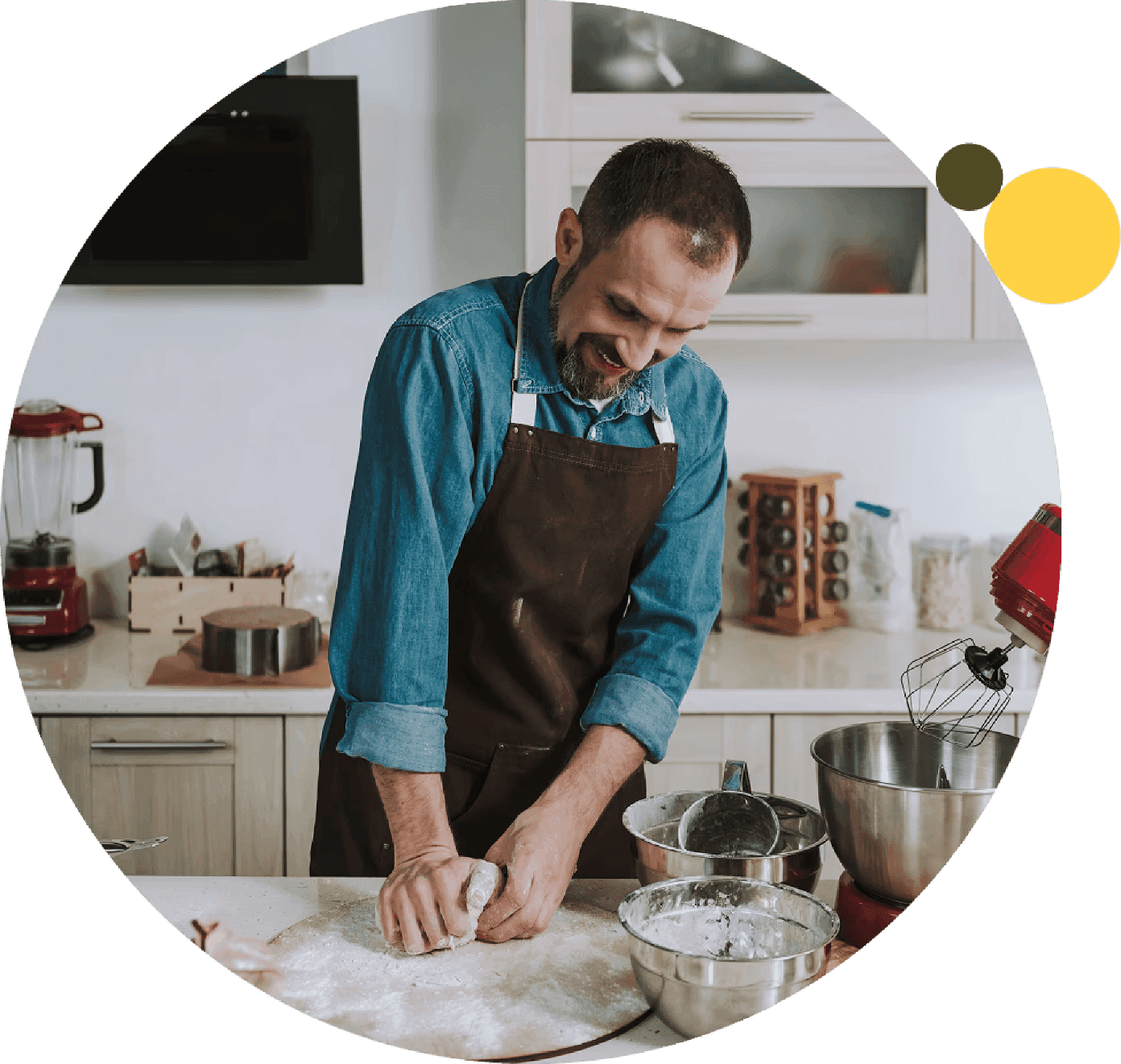 Man in an apron smiles while kneading dough on a floured countertop surrounded by baking tools