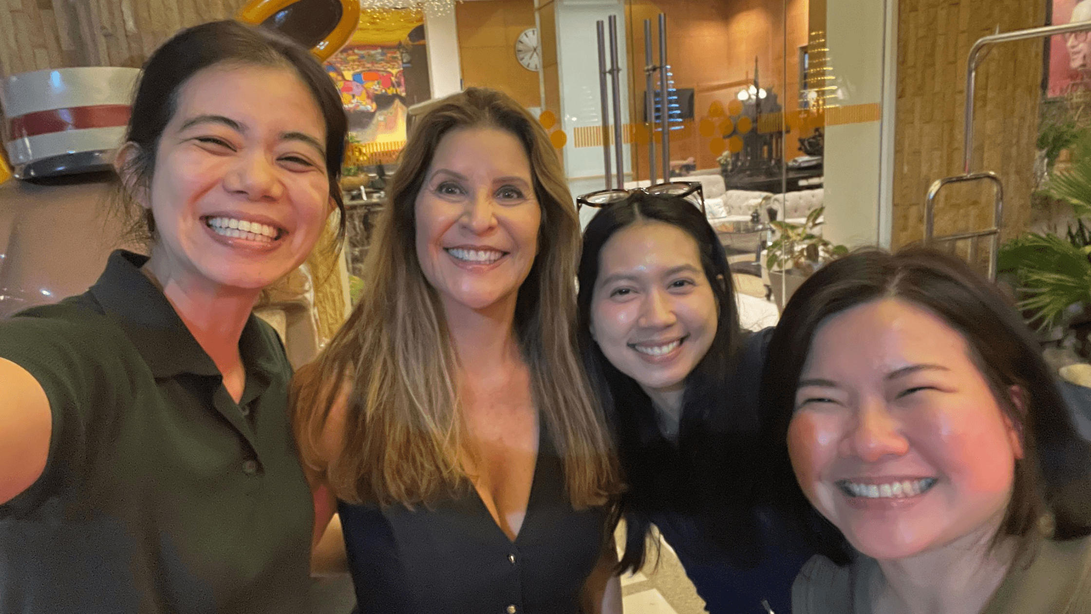 Four smiling women taking a group selfie together in a hotel lobby, celebrating a successful medical tourism trip.