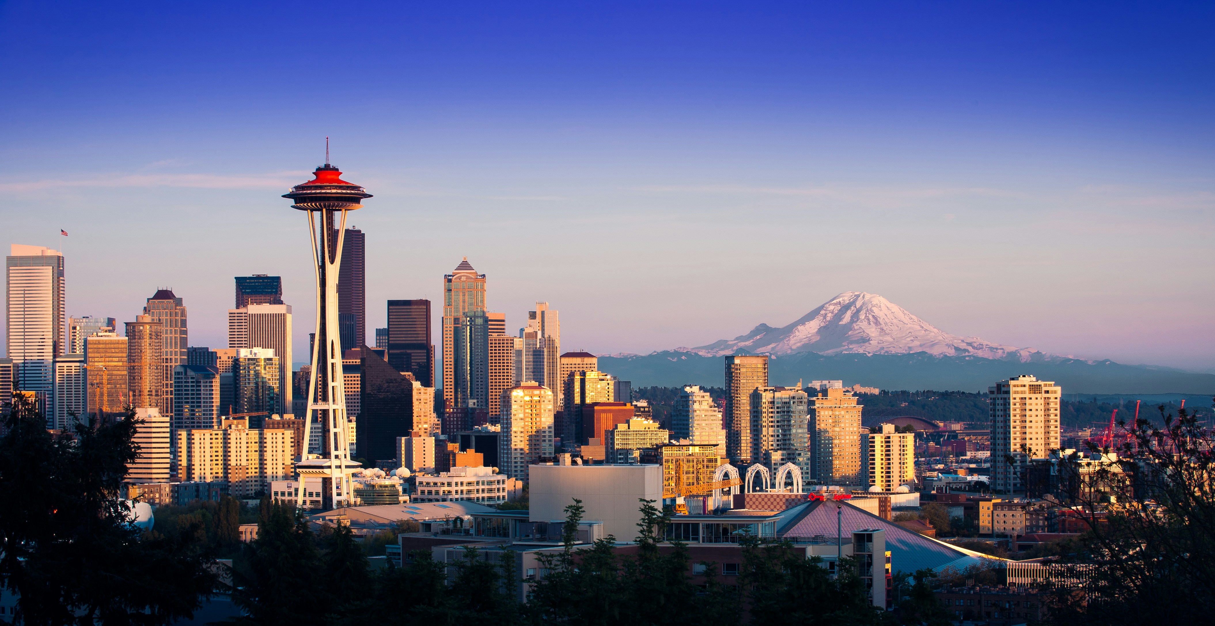 A skyline view of a city at dusk, featuring tall buildings and a prominent tower against a blue gradient sky.