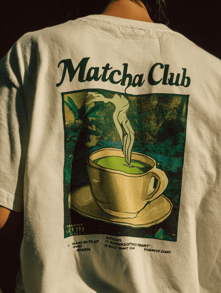 Back view of a person wearing a white T-shirt with a large graphic print featuring a steaming cup of matcha and the text “Matcha Club” above it.