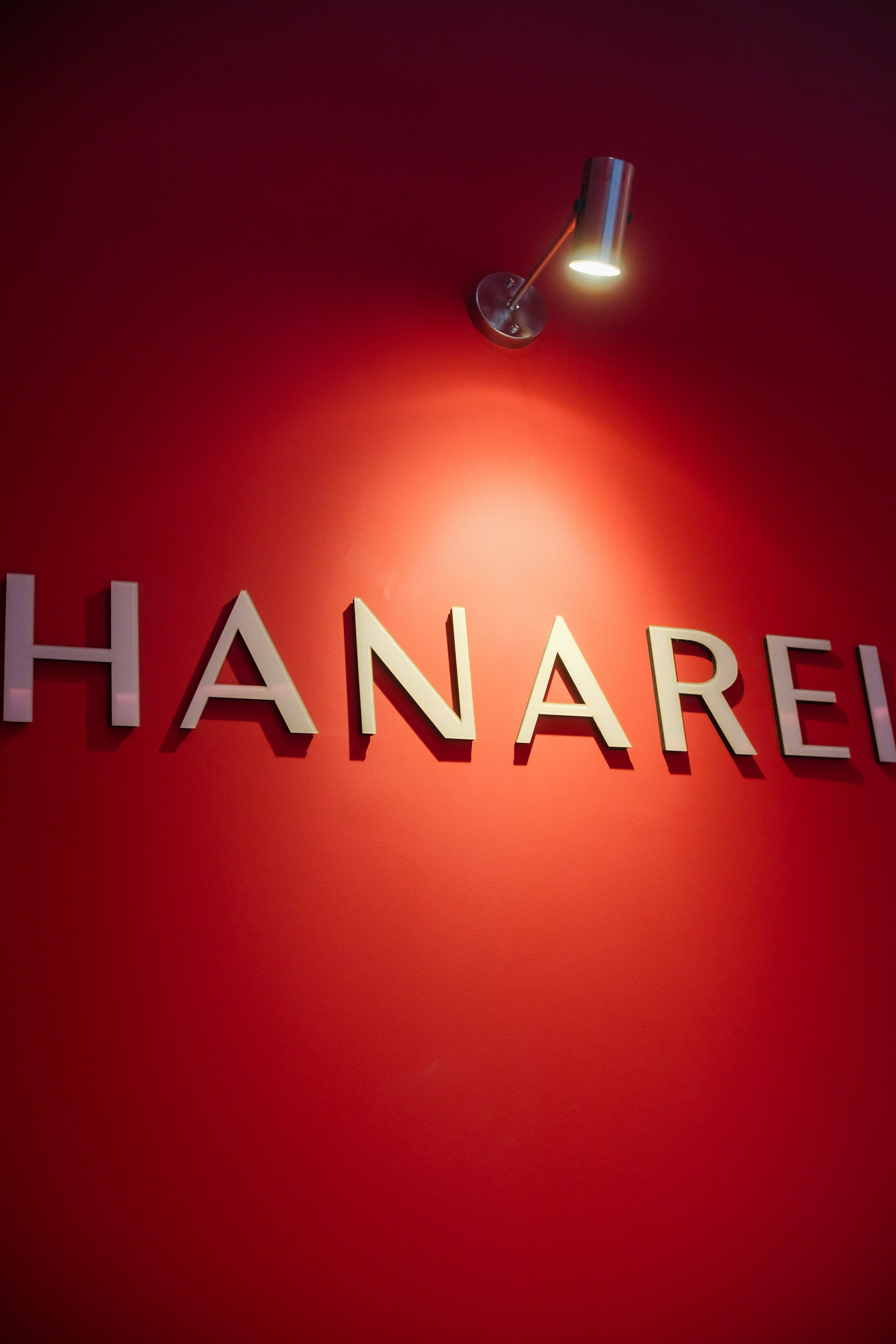 HANAREI nail salon sign on a red wall illuminated by a spotlight.
