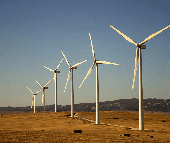 Row of wind turbines on a dry open landscape with hills in the background.
