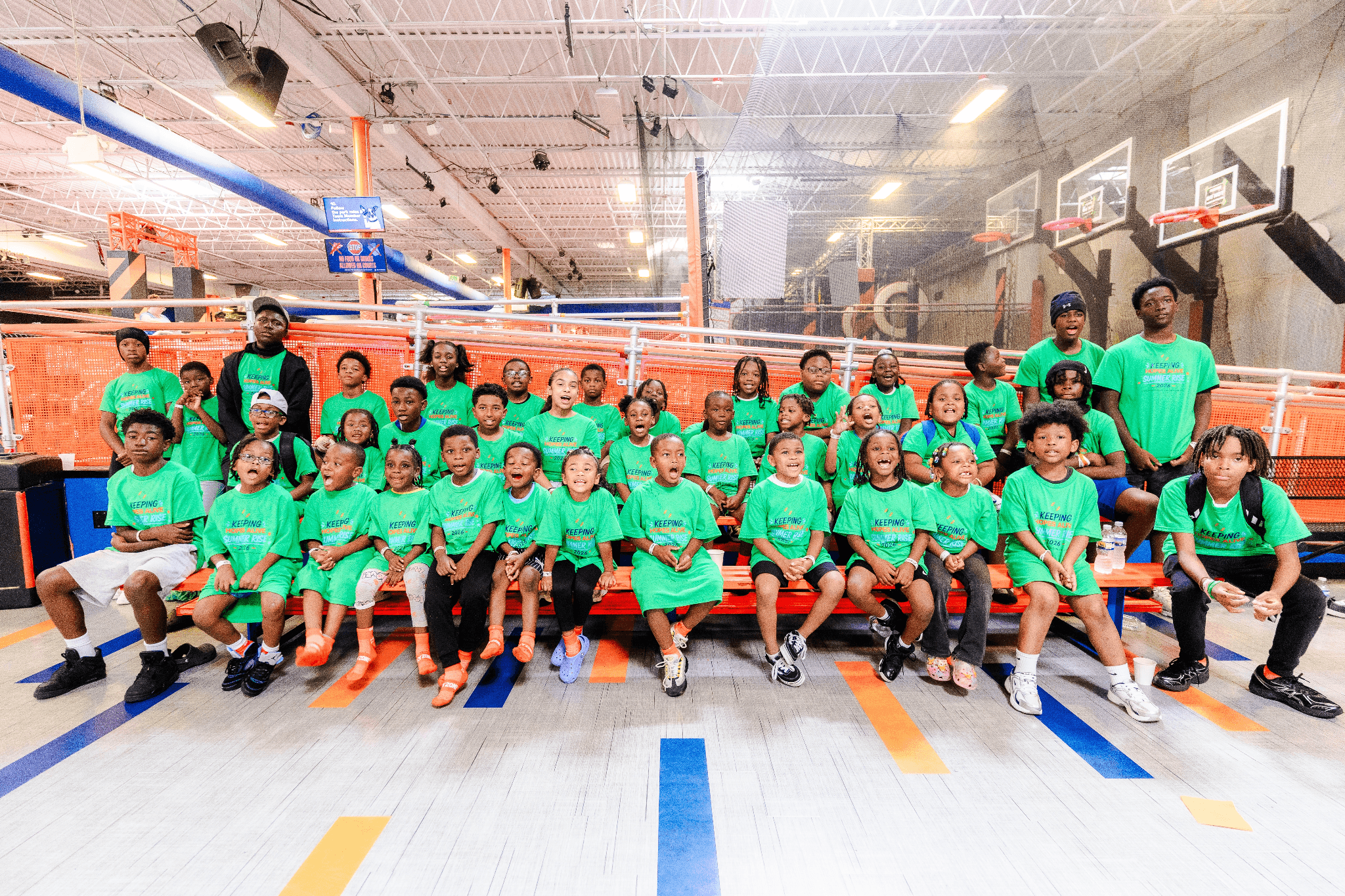Summer Rise participants in matching green shirts gather for a group photo at an indoor recreation center.