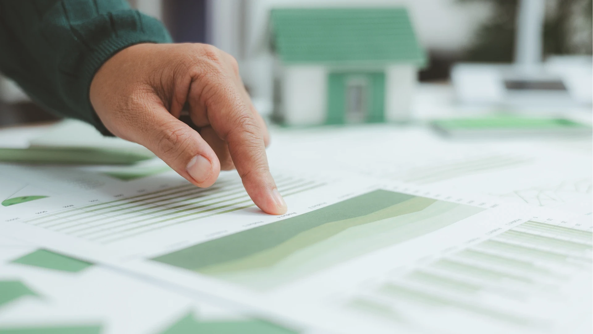 Detailaufnahme einer Hand, die auf grüne Daten-Diagramme einer ERP-Prozessanalyse zeigt. Im Hintergrund ein Modellhaus als Symbol für nachhaltiges Bauen und ESG-Reporting im Mittelstand. Die Grafik verdeutlicht die ERP-Implementierung, Prozessoptimierung und den digitalen CO2-Fußabdruck in der Branchensoftware 2026.