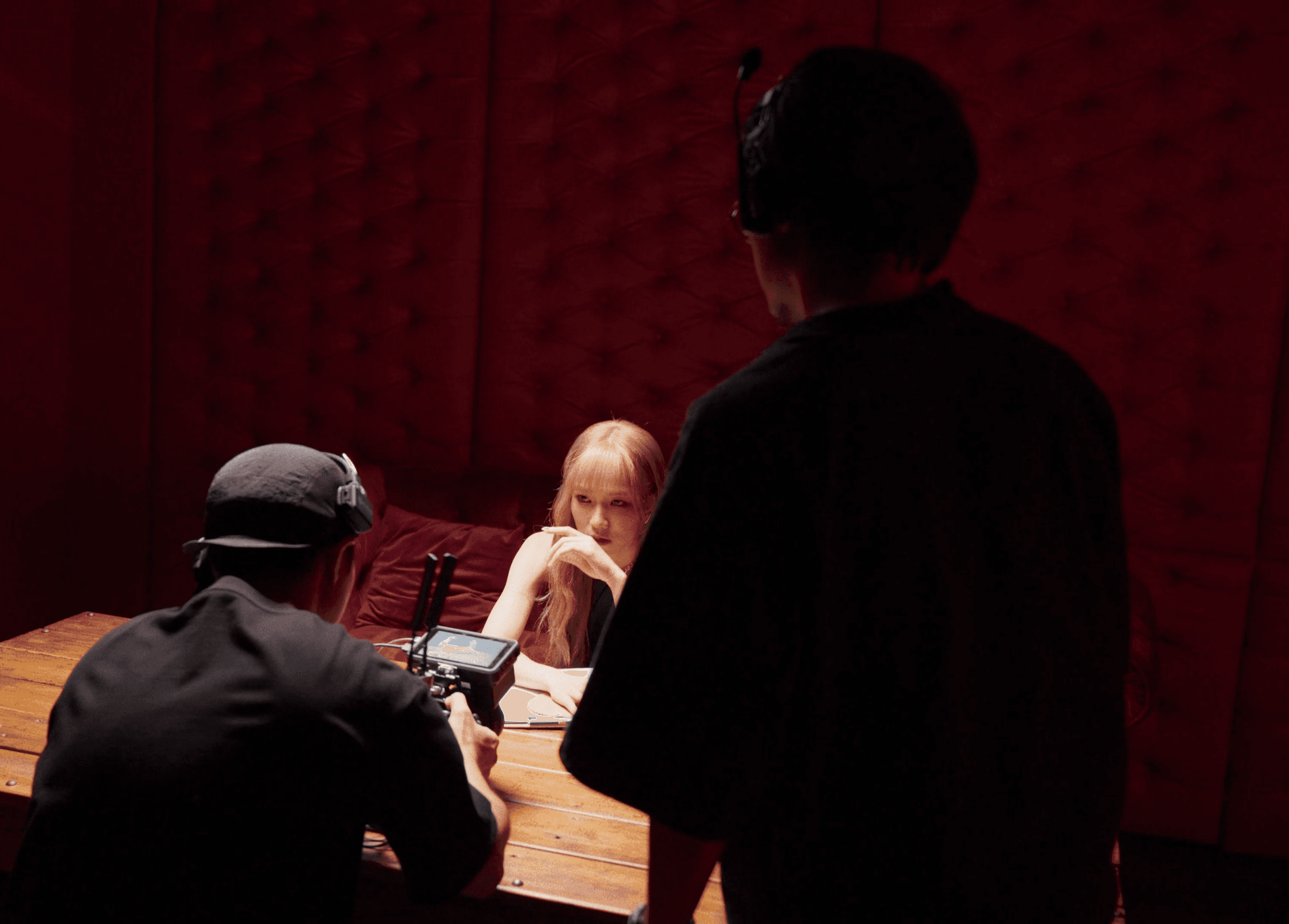 A film director sits in a chair facing a bustling, warmly lit night market scene. A camera setup is nearby, capturing the energetic atmosphere.