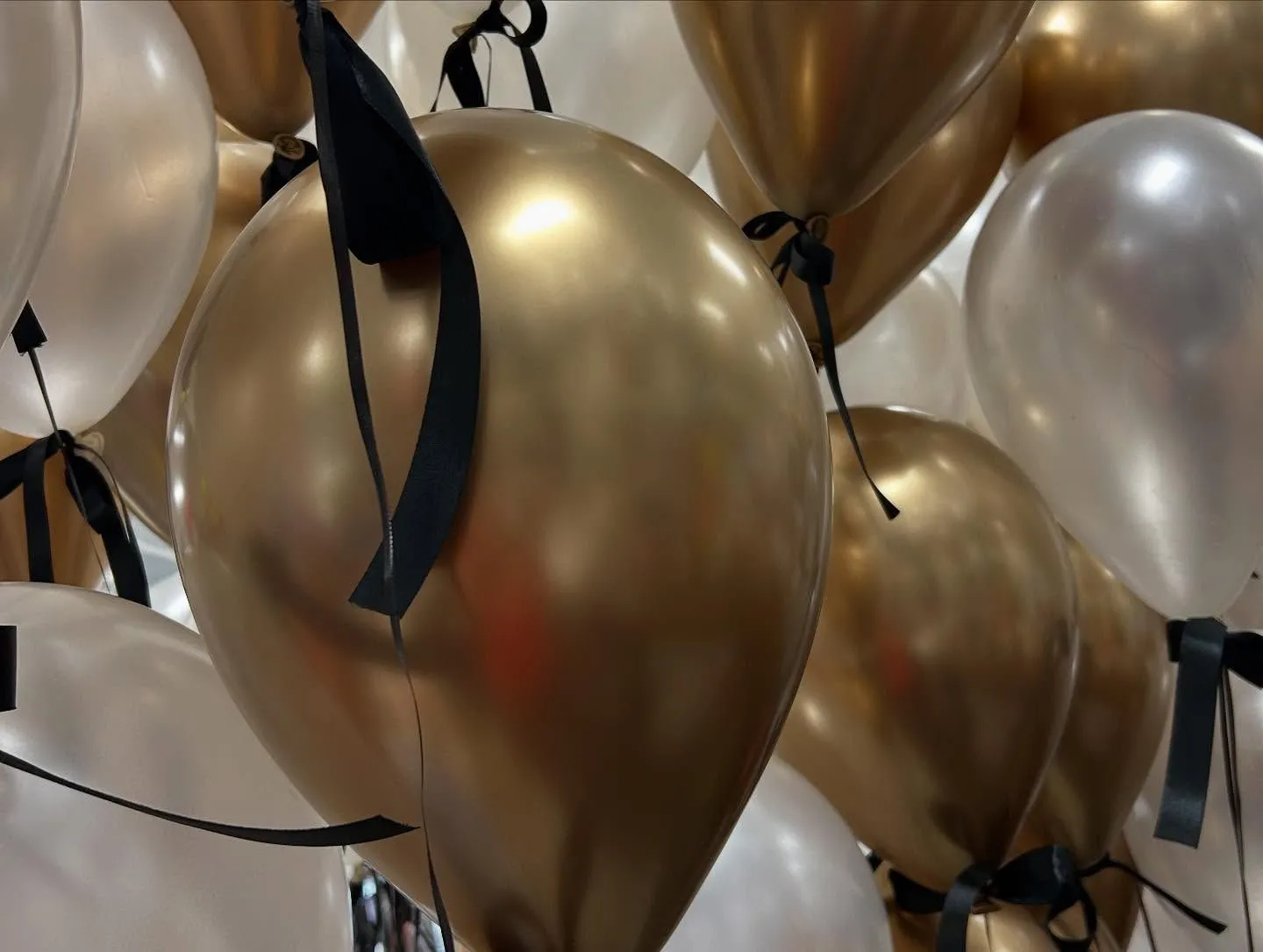 A cluster of gold and white balloons with black ribbons creates an elegant and festive atmosphere, perfect for celebrations or special events.