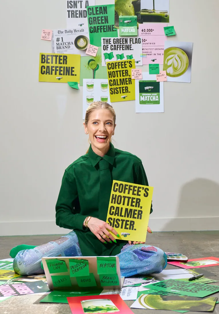 Marisa Poster sitting among campaign boards, holding a "Coffee's hotter, calmer sister" sign