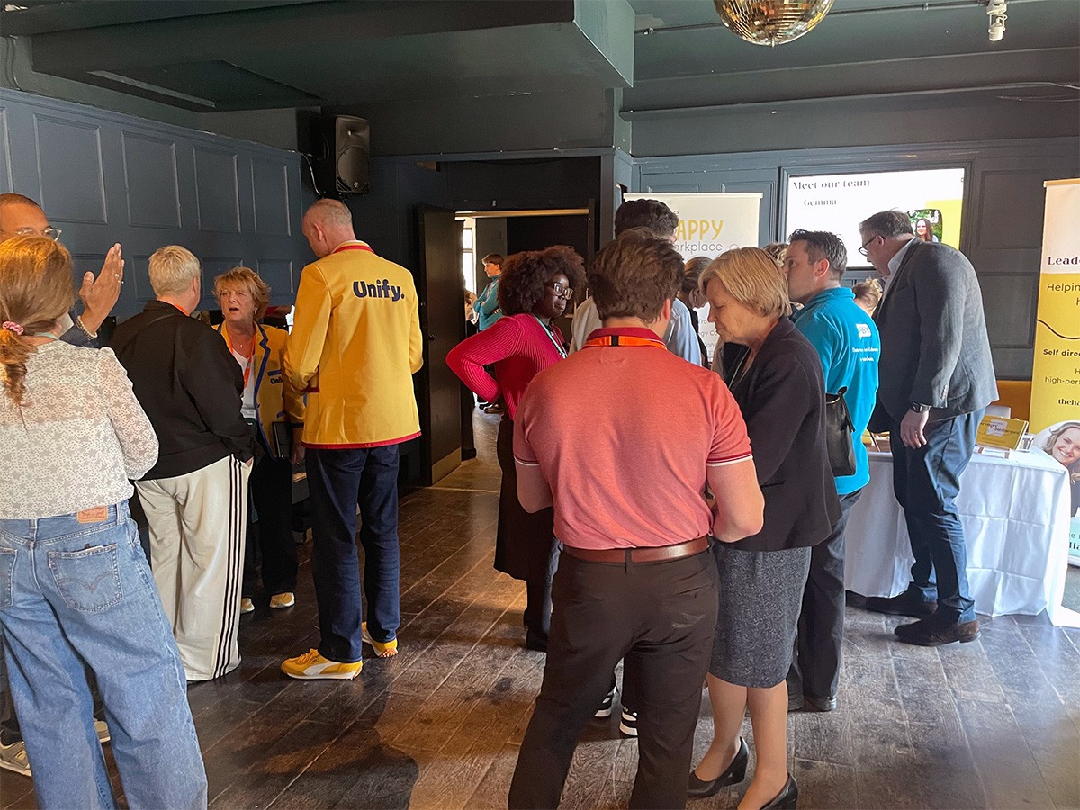 Attendees networking during the HubGem LIVE! event at Exhibit, Balham, with sponsor stands including Unify and Happy Workplace visible in the background