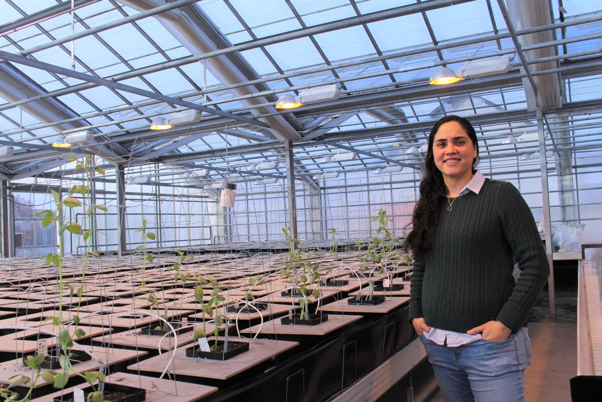 A Latina woman standing in a greenhouse smiling
