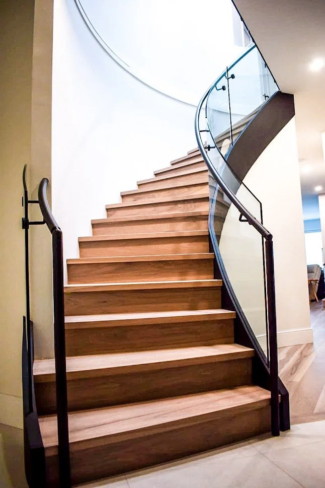 Curved modern glass stair railing on a curved wood staircase with dark handrail and frameless glass panels.
