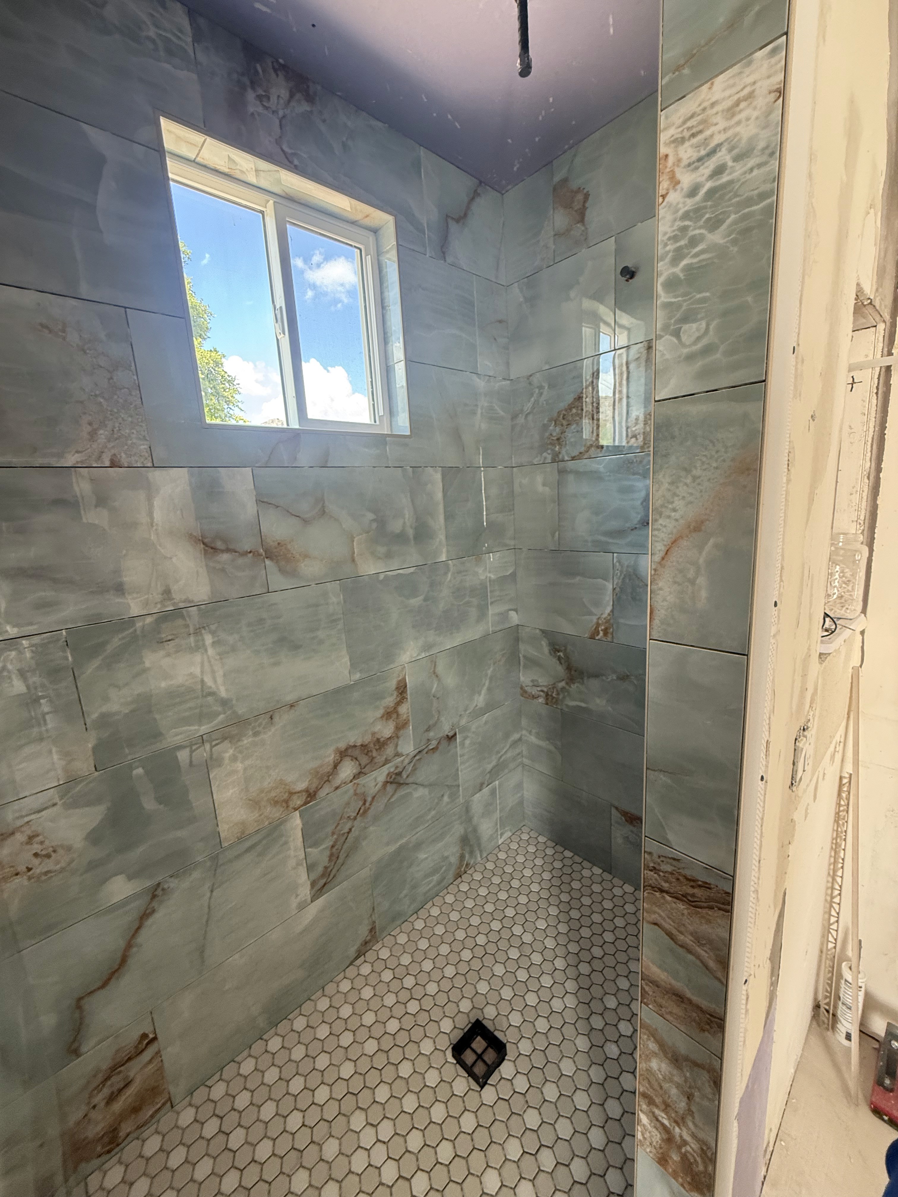Bathtub shower combo with sleek grey marble-look large format wall tiles, a built-in shower niche with a white and grey hexagonal mosaic tile accent, and modern chrome fixtures.