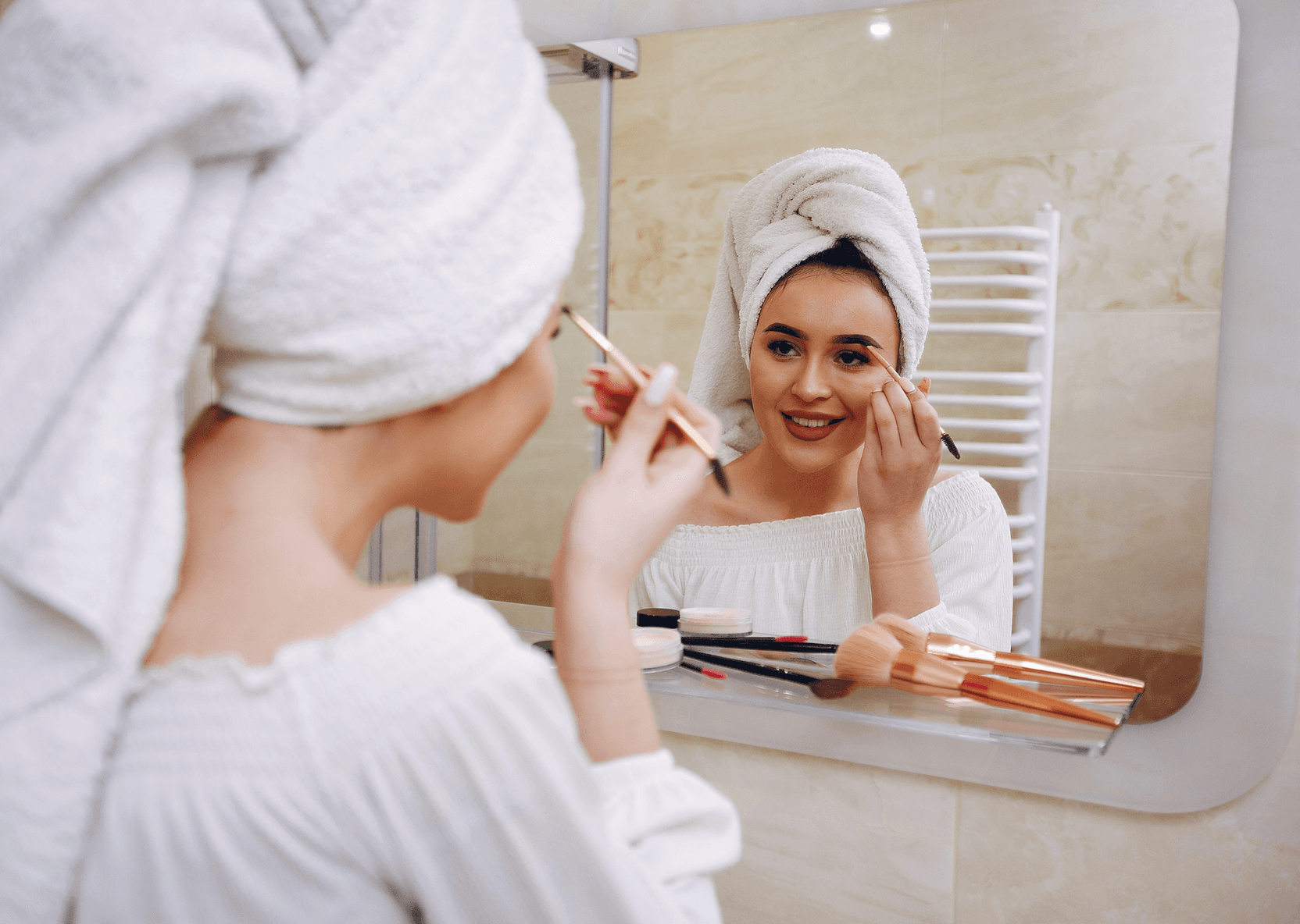 Woman in a towel doing her eyebrows.