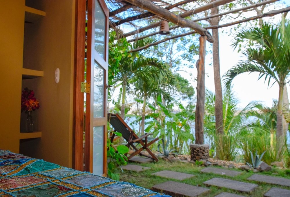 View from a bedroom doorway looking out onto a garden with a lounge chair and palm trees.