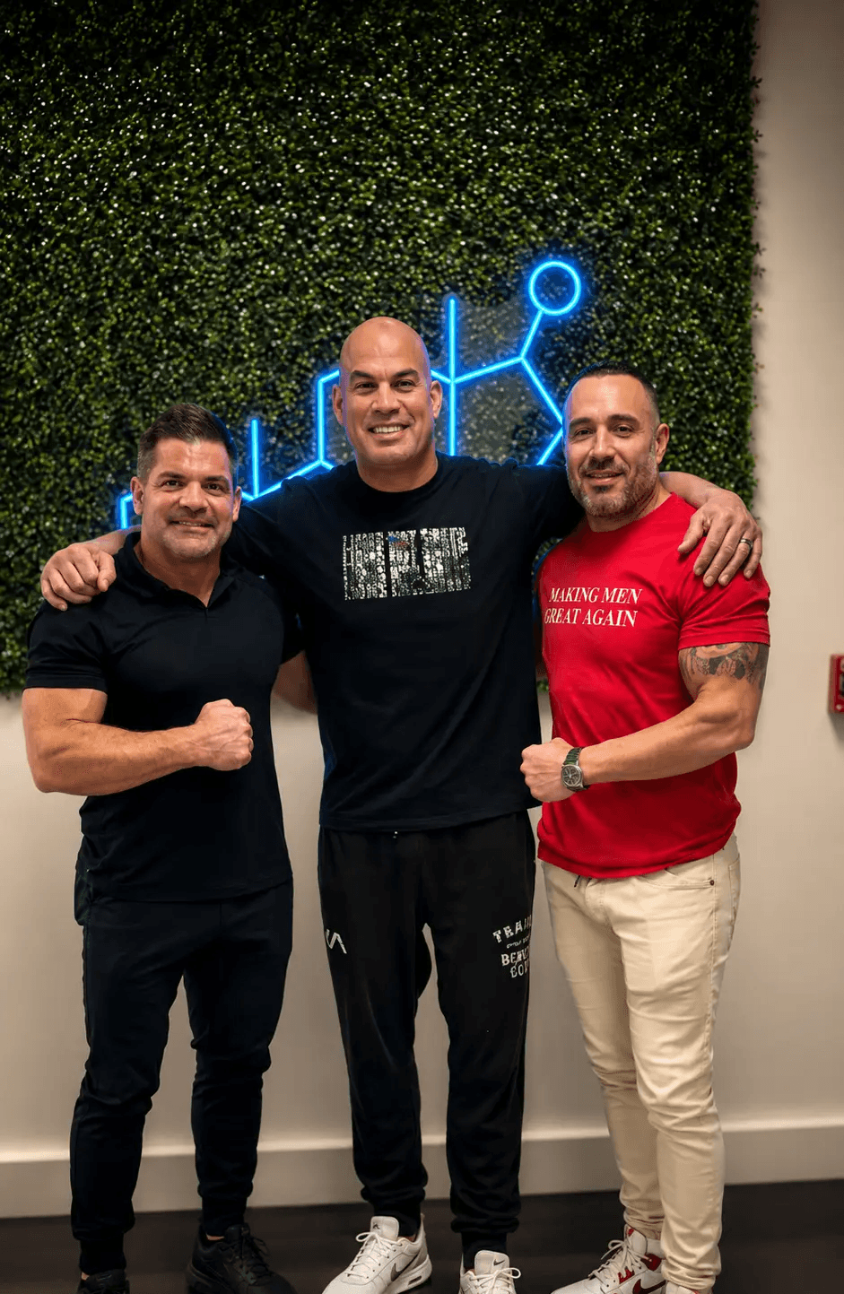 Three men posing together in front of a T Clinics USA logo wall