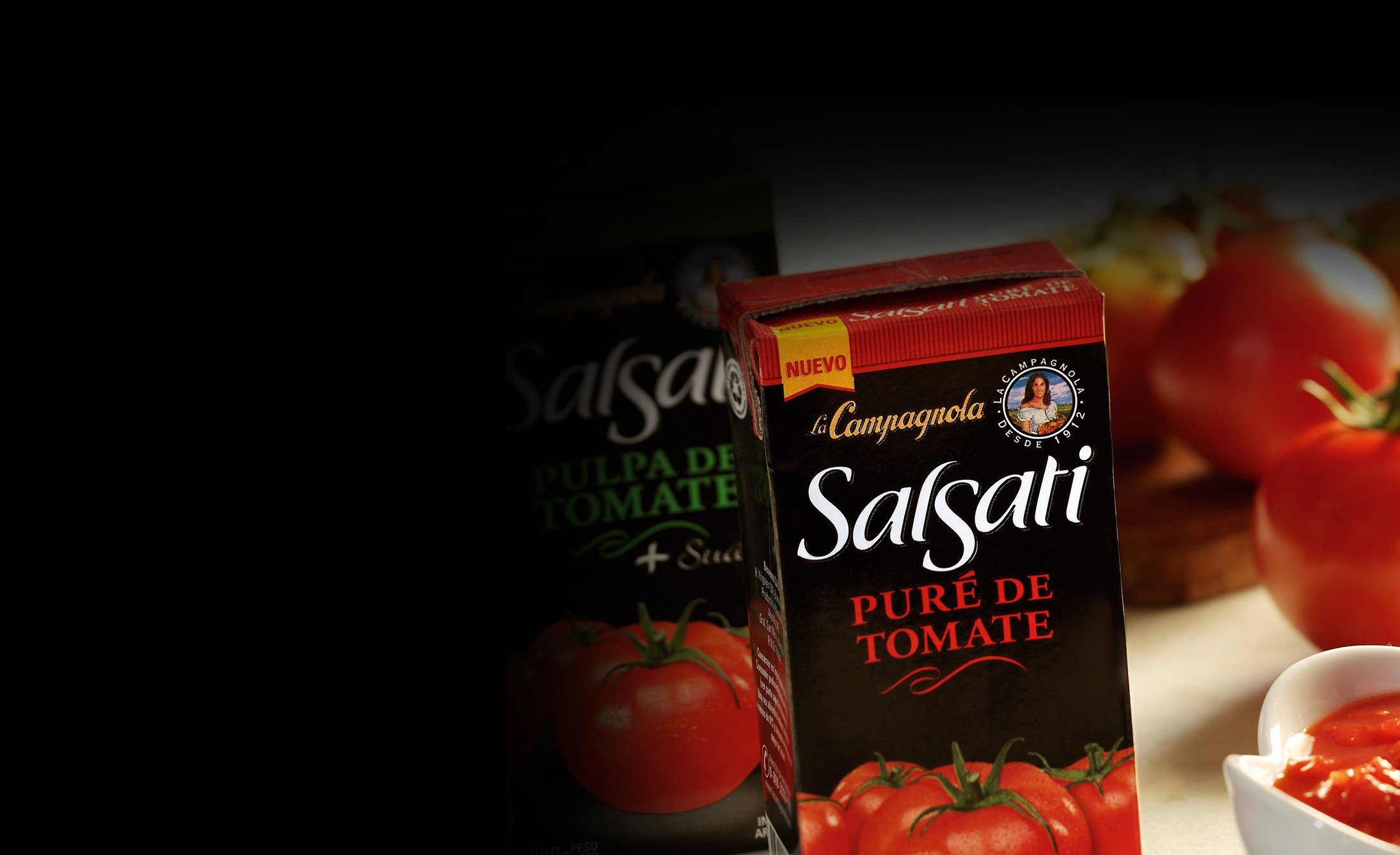 Box of "Salsati Puré de Tomate" in the foreground on a wooden surface with fresh tomatoes and a sauce bowl. The tone is appetizing and inviting.