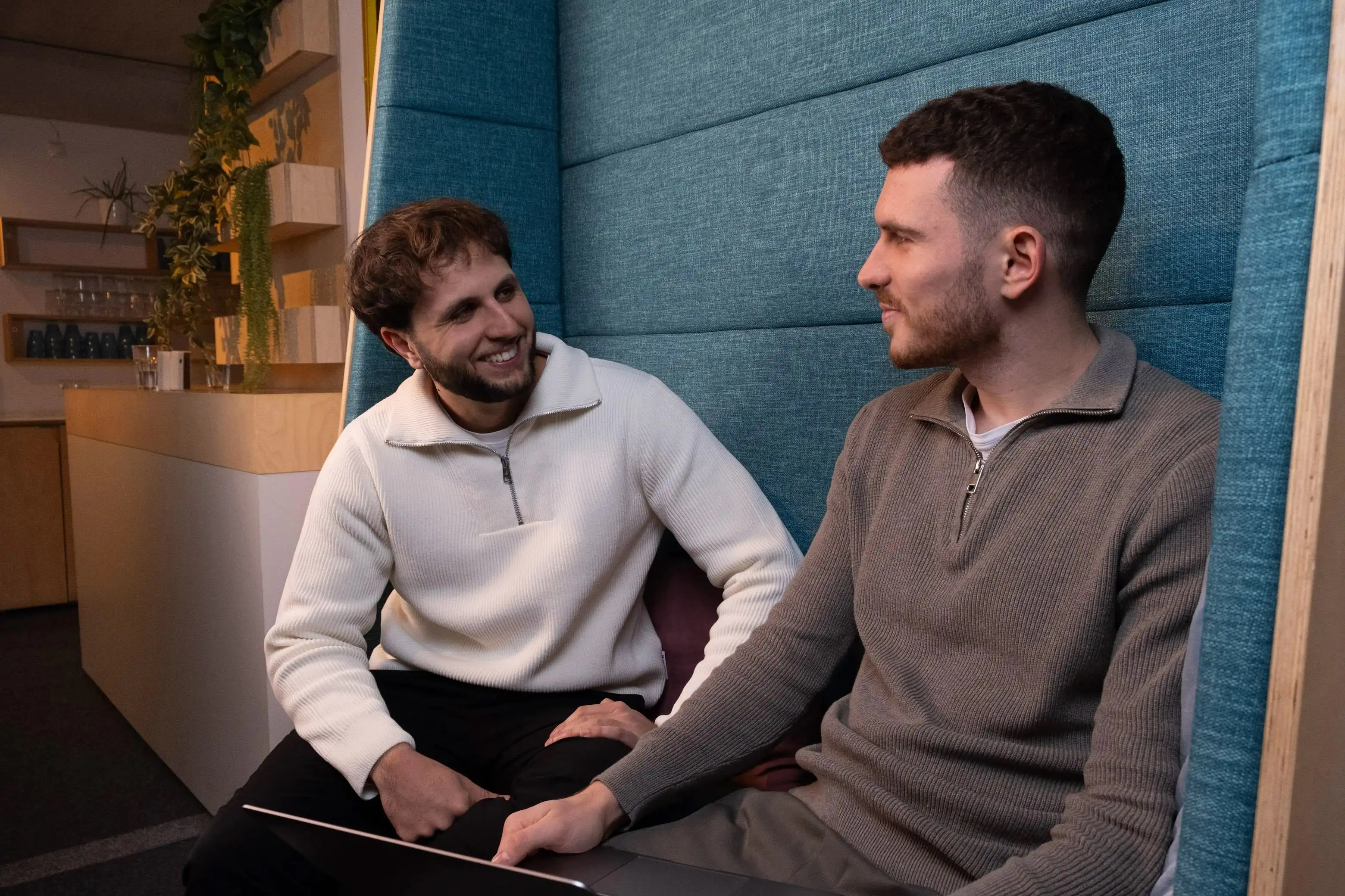 Two men sitting together, engaged in conversation, with a colorful background adding a cozy vibe.