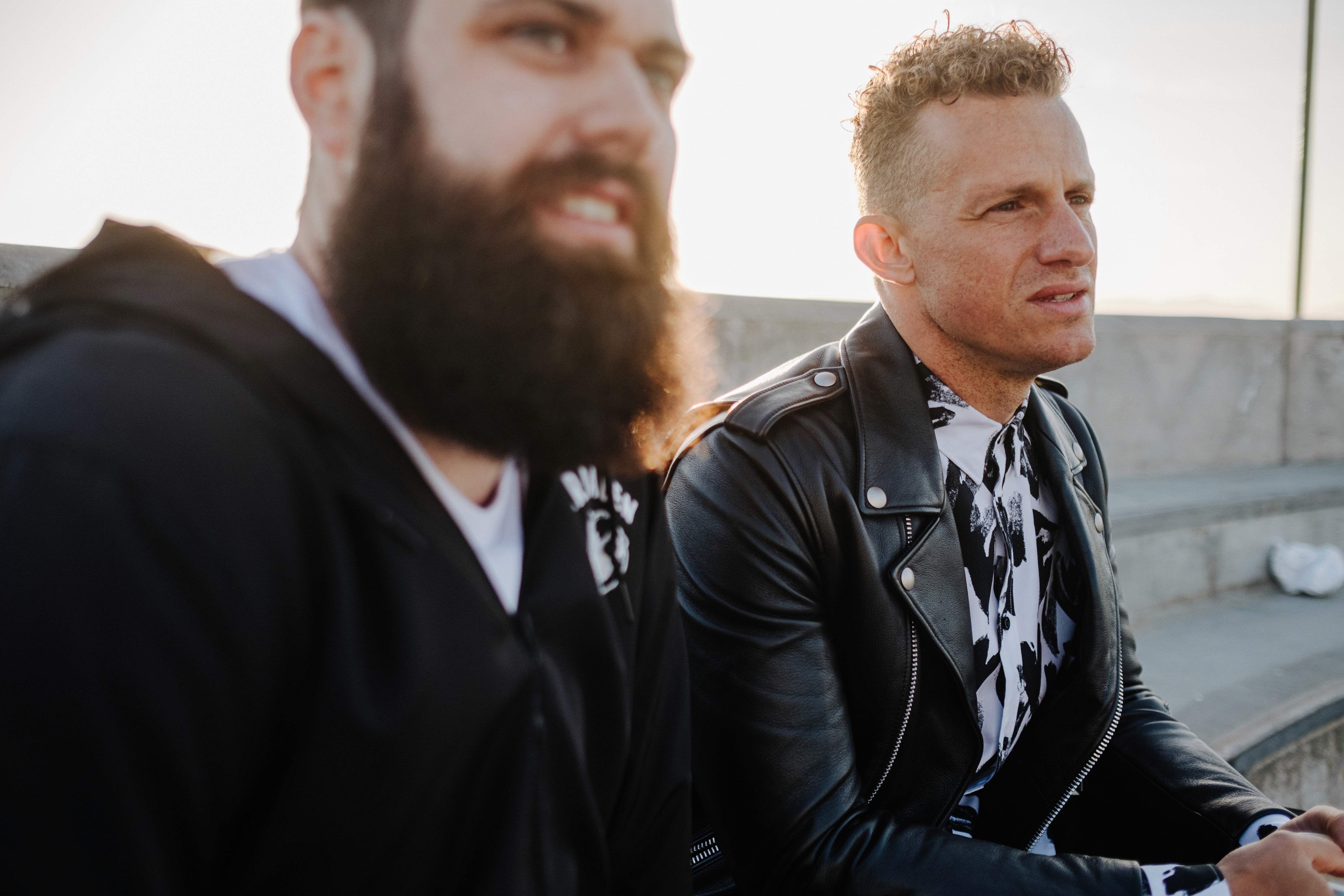 two men with serious facs looking away from the camera with the sun behind them