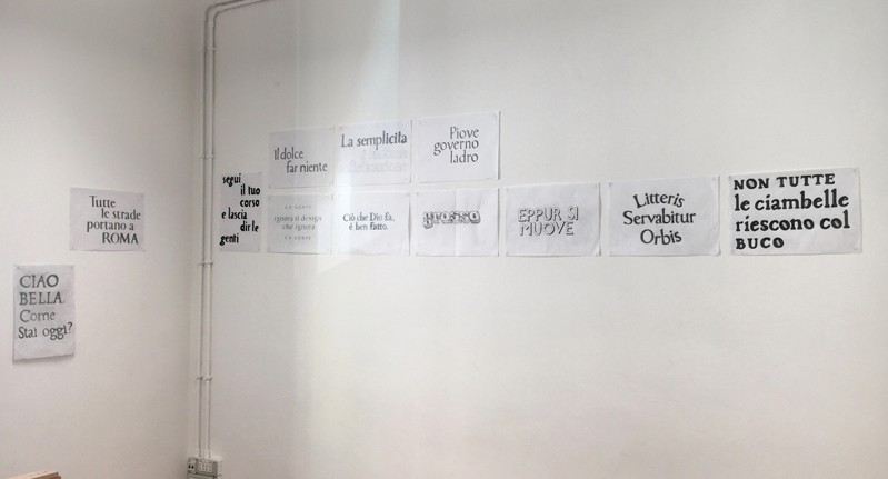 A photo of some sample papers glued on the wall. Each paper has some typographical letters drawn by students in multiple styles.
