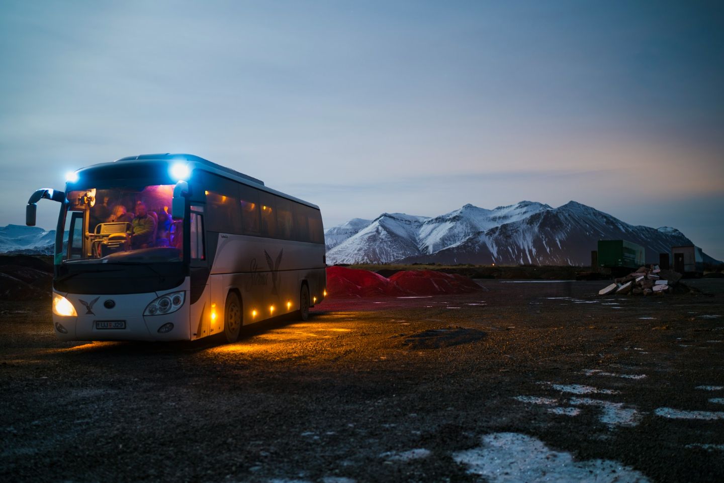 Guided tour bus parked near snow-covered mountains in Iceland during the evening.